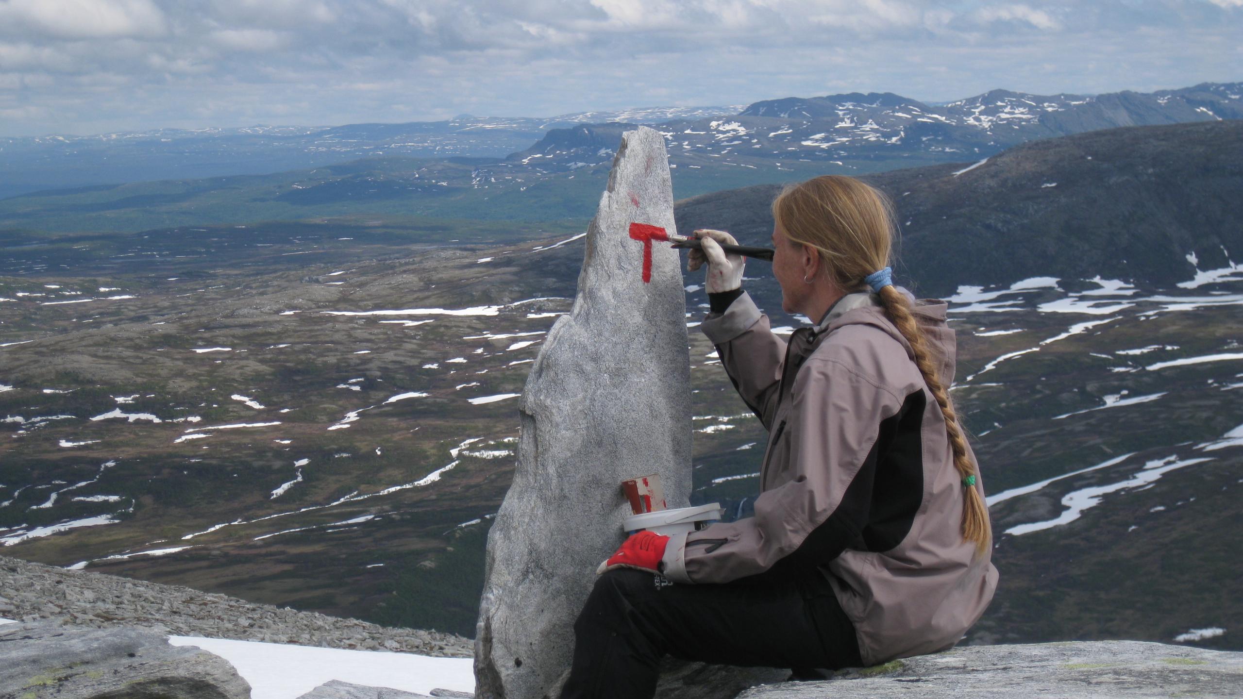 Jorid Rajala of DNT, painting signs along a hiking trail with a nice mountain view in the background