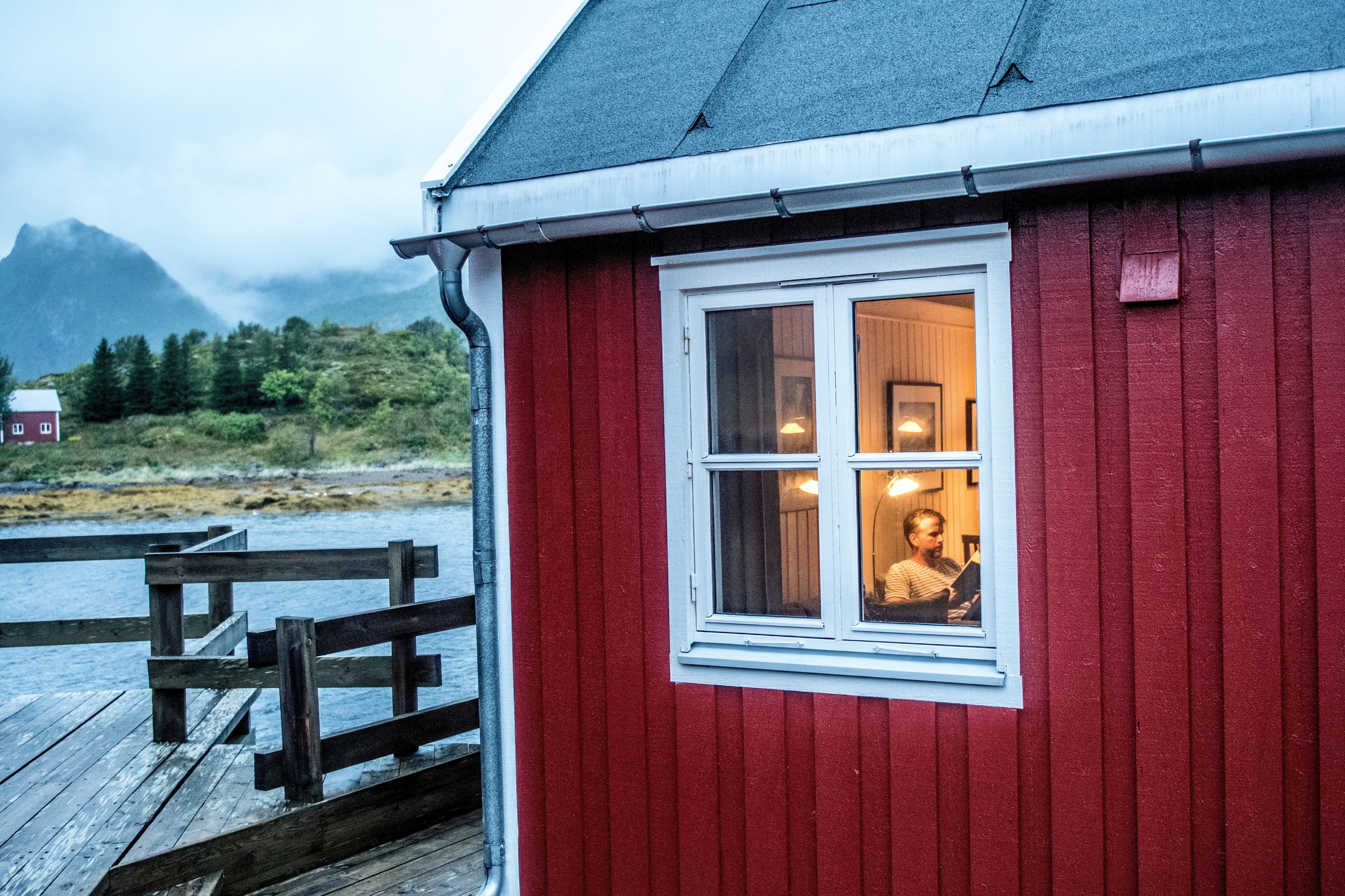 En mann sitter inne og leser i en rorbu i Lofoten, Nord-Norge