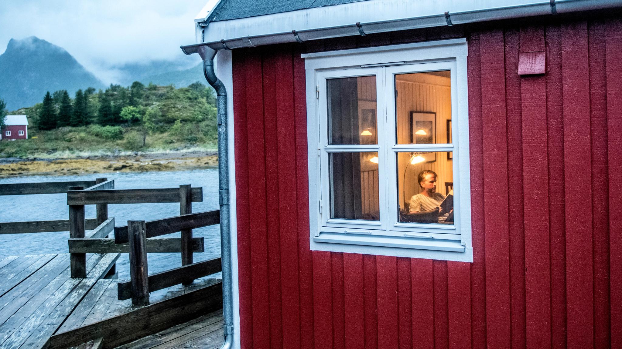 En mann sitter inne og leser i en rorbu i Lofoten, Nord-Norge
