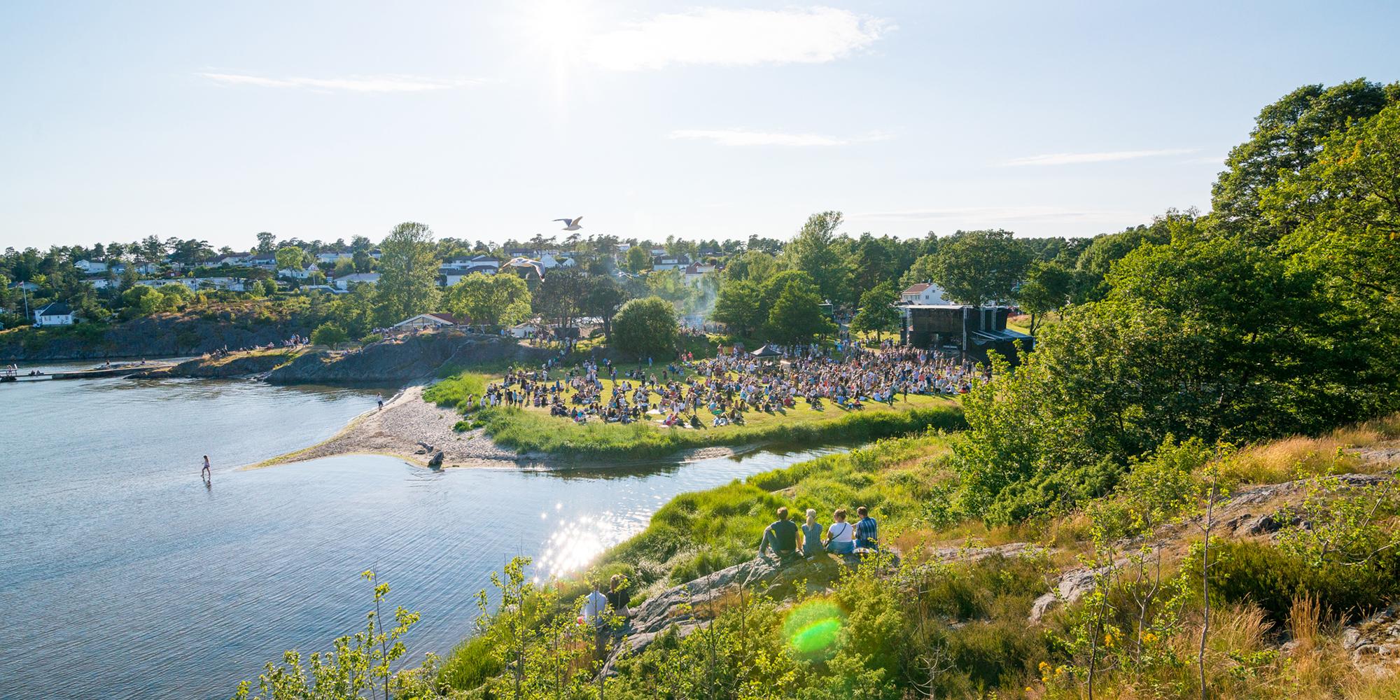 Menschen sitzen auf dem Rasen am Meer während des Skral Festivals in Grimstad in Südnorwegen