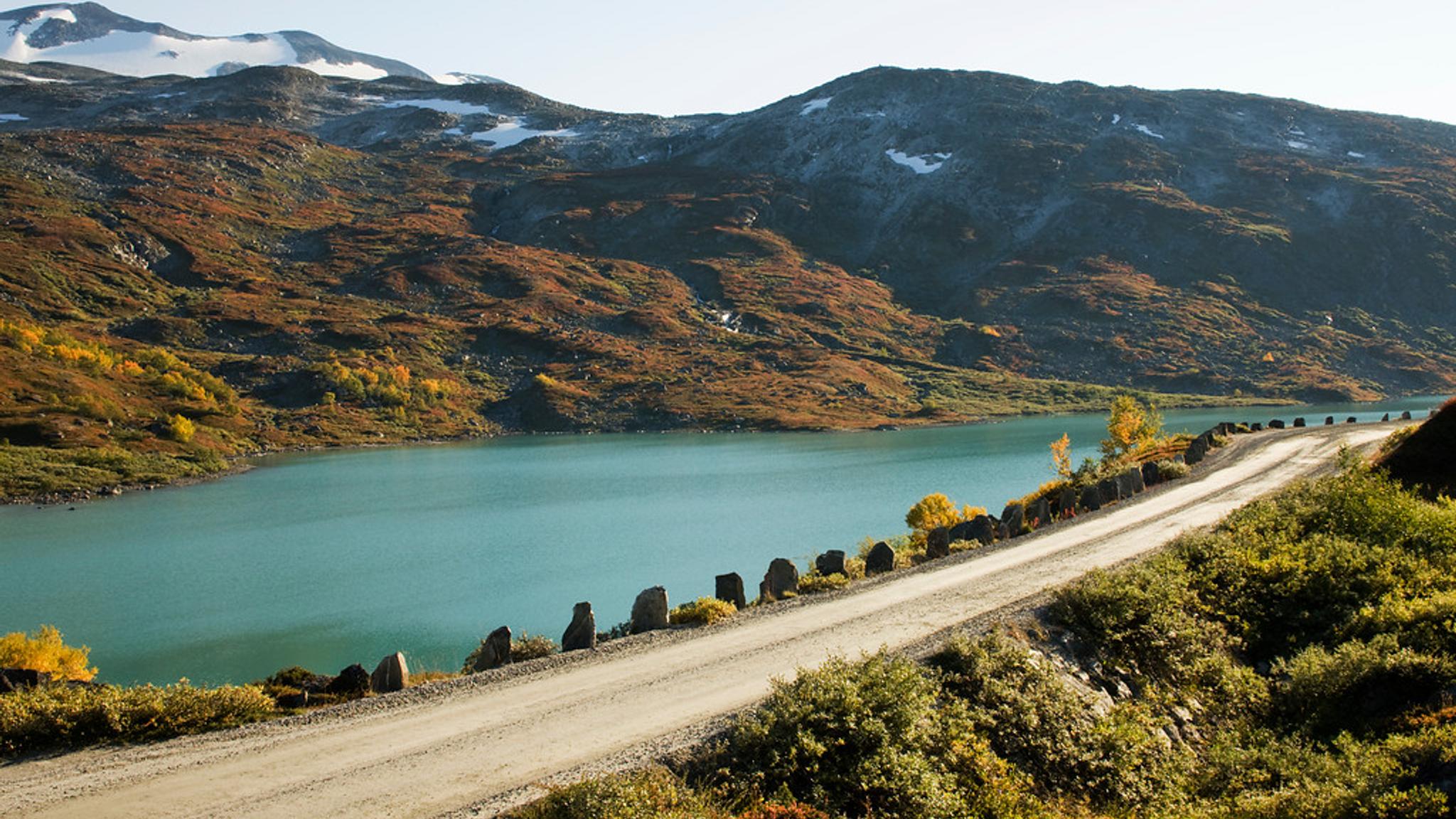 A road right next to a bright blue lake.