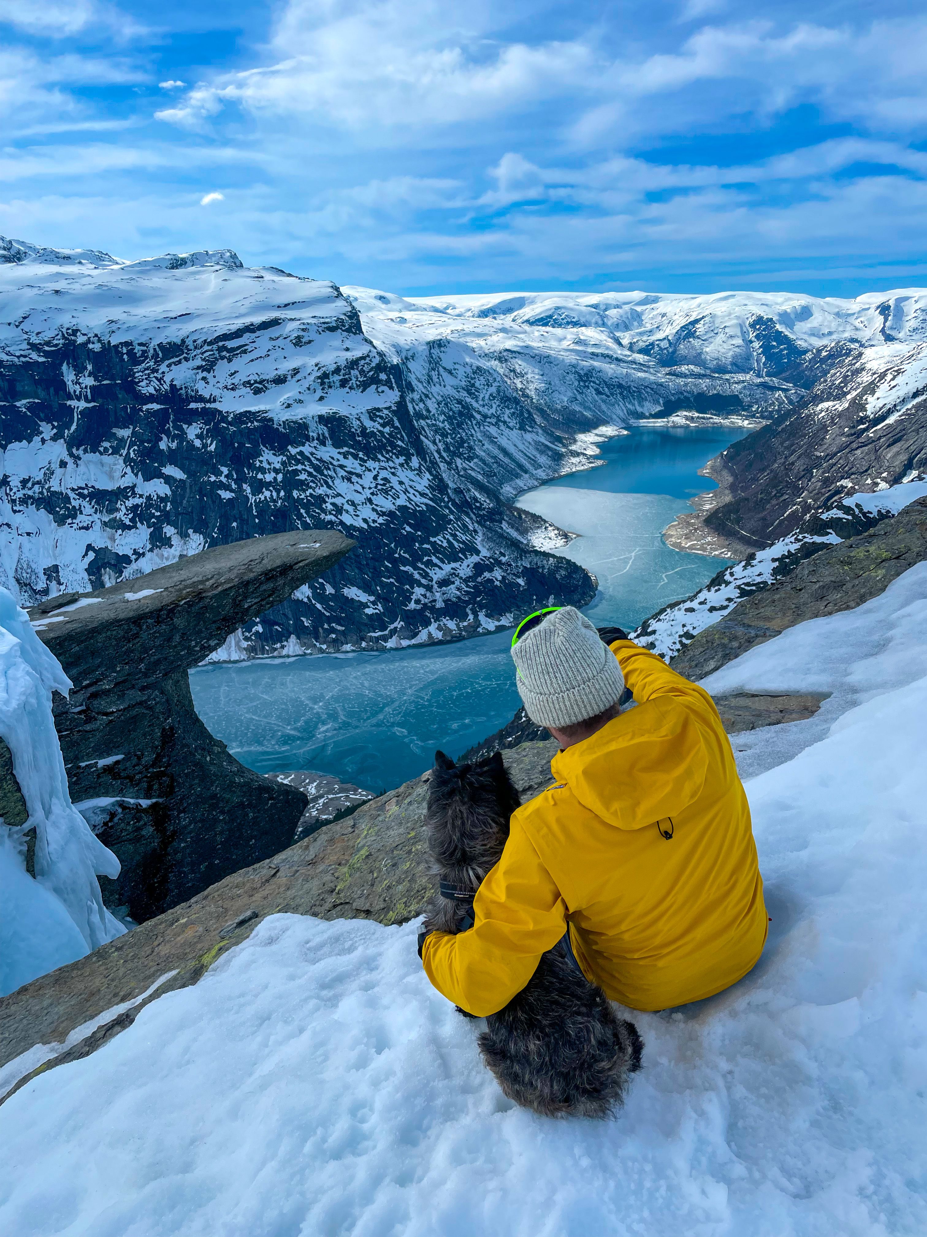 En mann og en hund som ser på Trolltunga fjellformasjonen på vinteren.