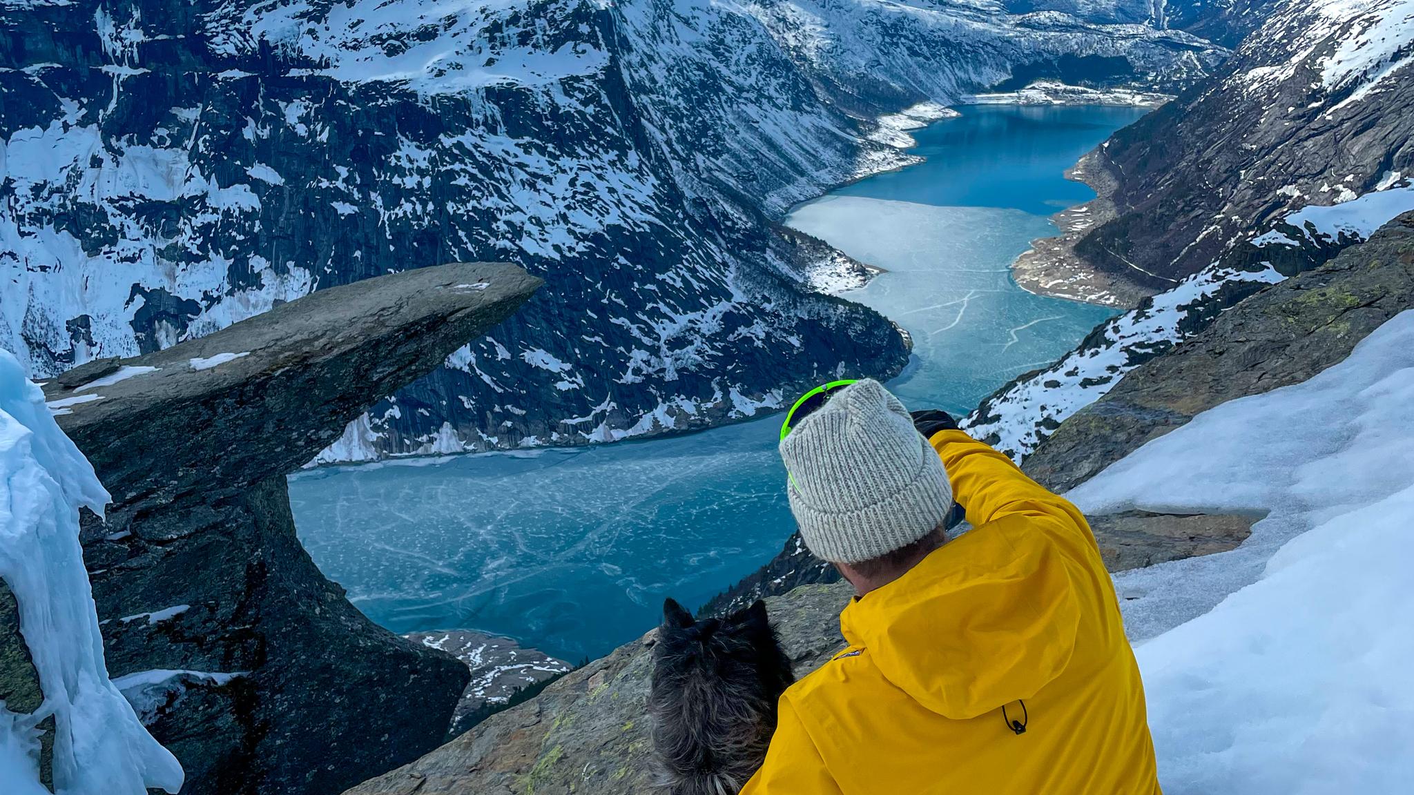 En mann og en hund som ser på Trolltunga fjellformasjonen på vinteren.