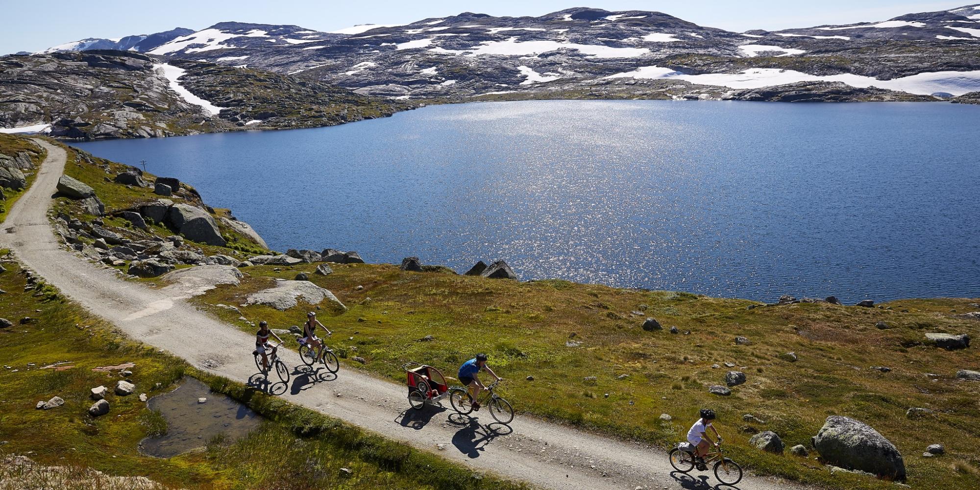 En gruppe syklister sykler langs en innsjø på Rallarvegen i Norge