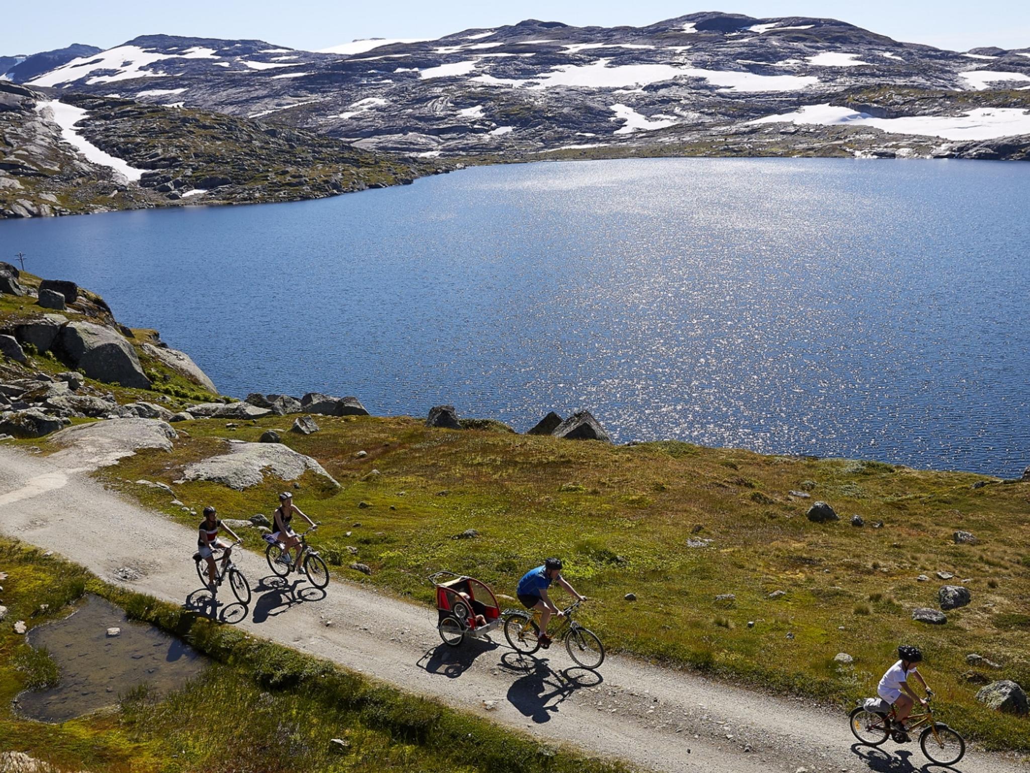 En gruppe syklister sykler langs en innsjø på Rallarvegen i Norge