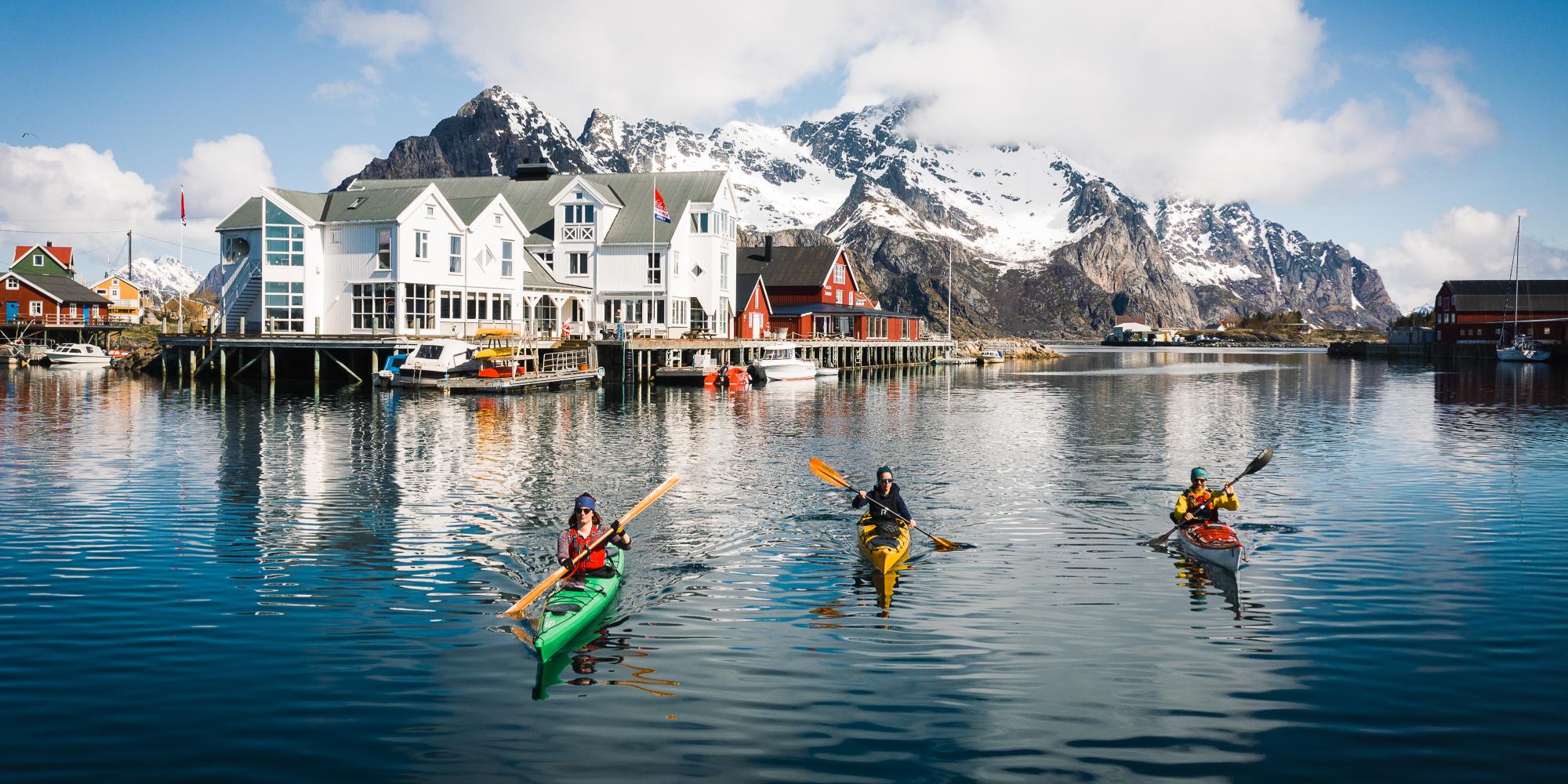 People winter kayaking by the Henningsvær Bryggehotell in Lofoten, Northern Norway.