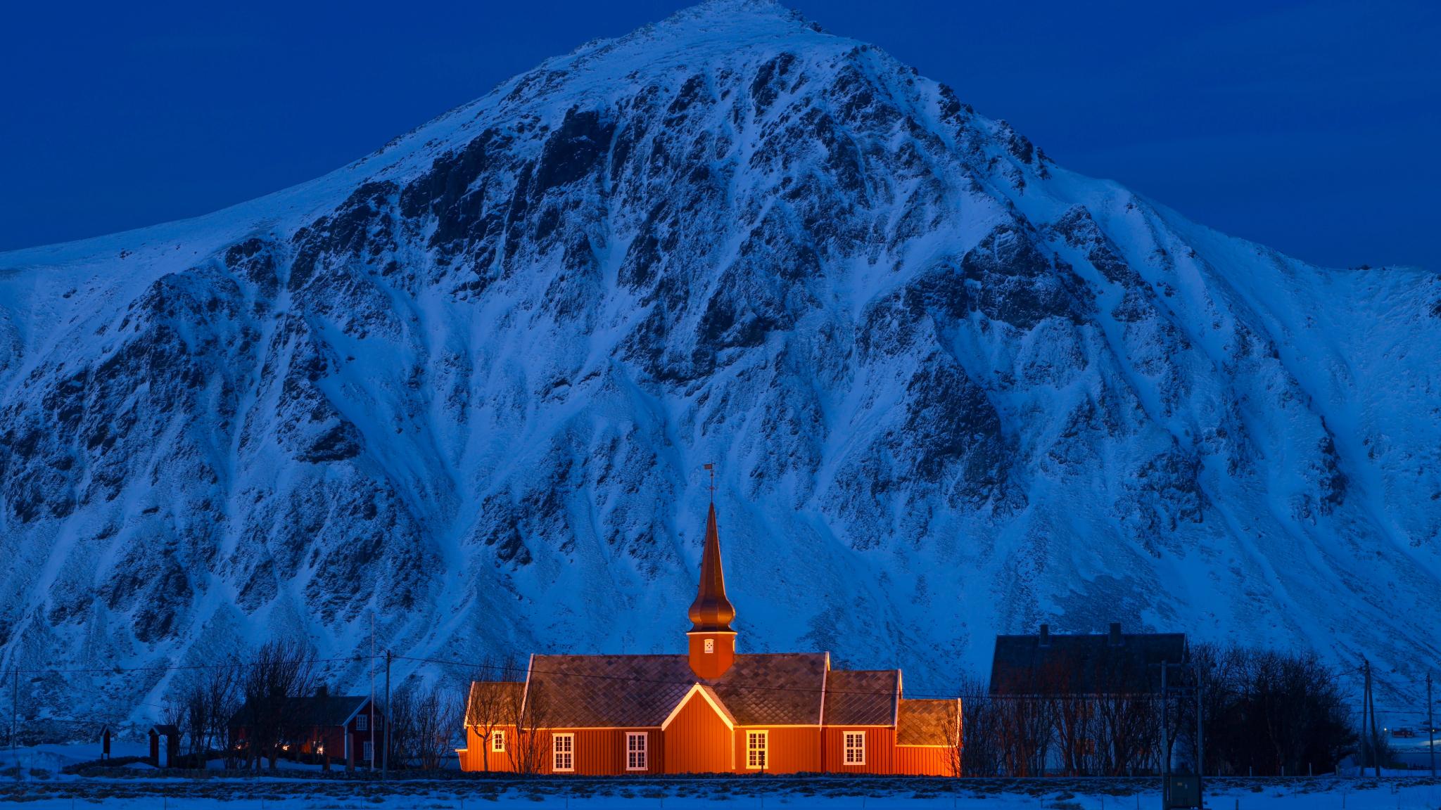 A lit up church in front of a steep mountain.