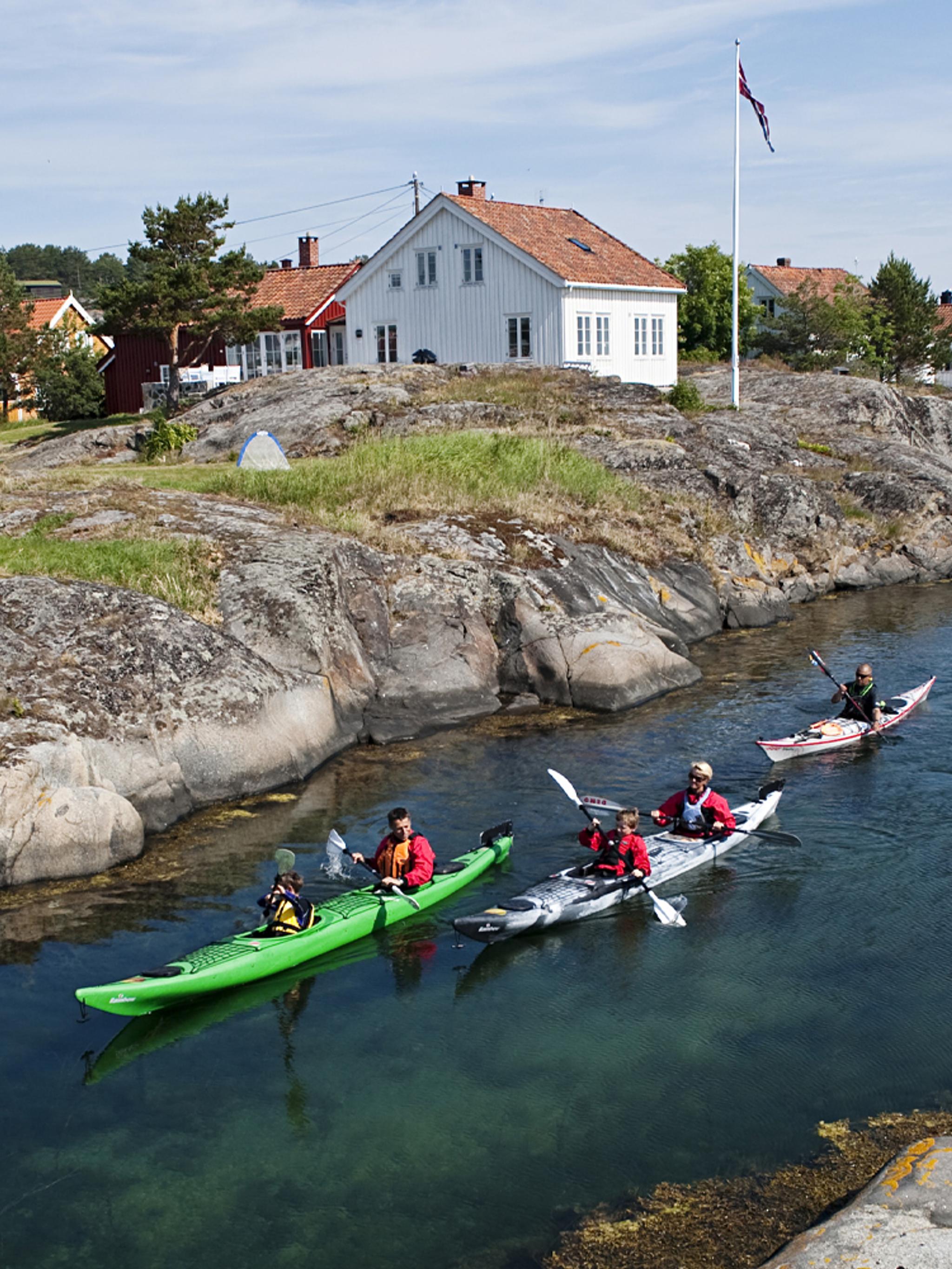 Drei Kajaks durchqueren eine Meeresstraße zwischen den Inseln von Risør, Südnorwegen