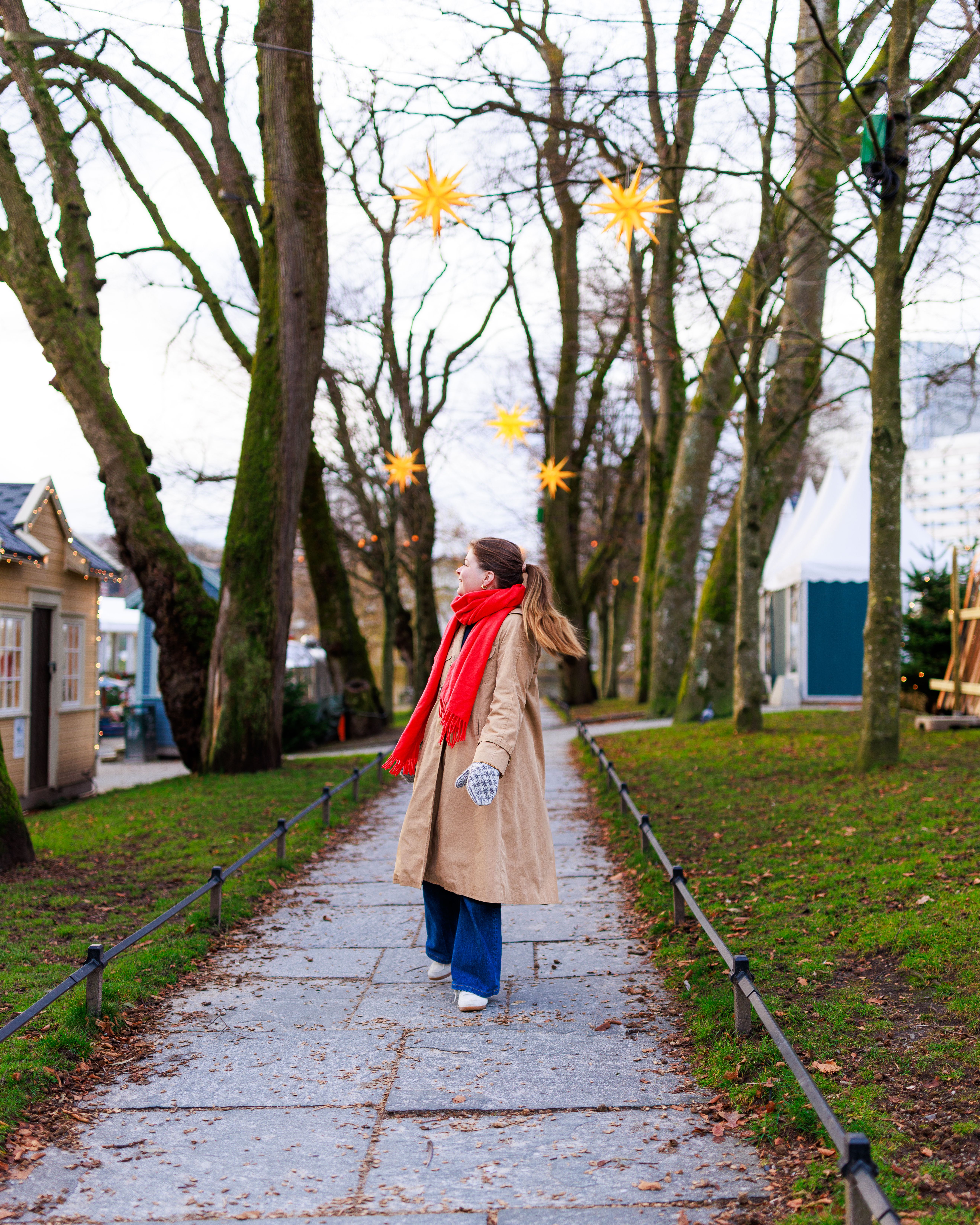 A woman strolling along a path in Stavanger, surrounded by trees decorated with yellow star-shaped lights, adding a festive, Christmas ambiance.