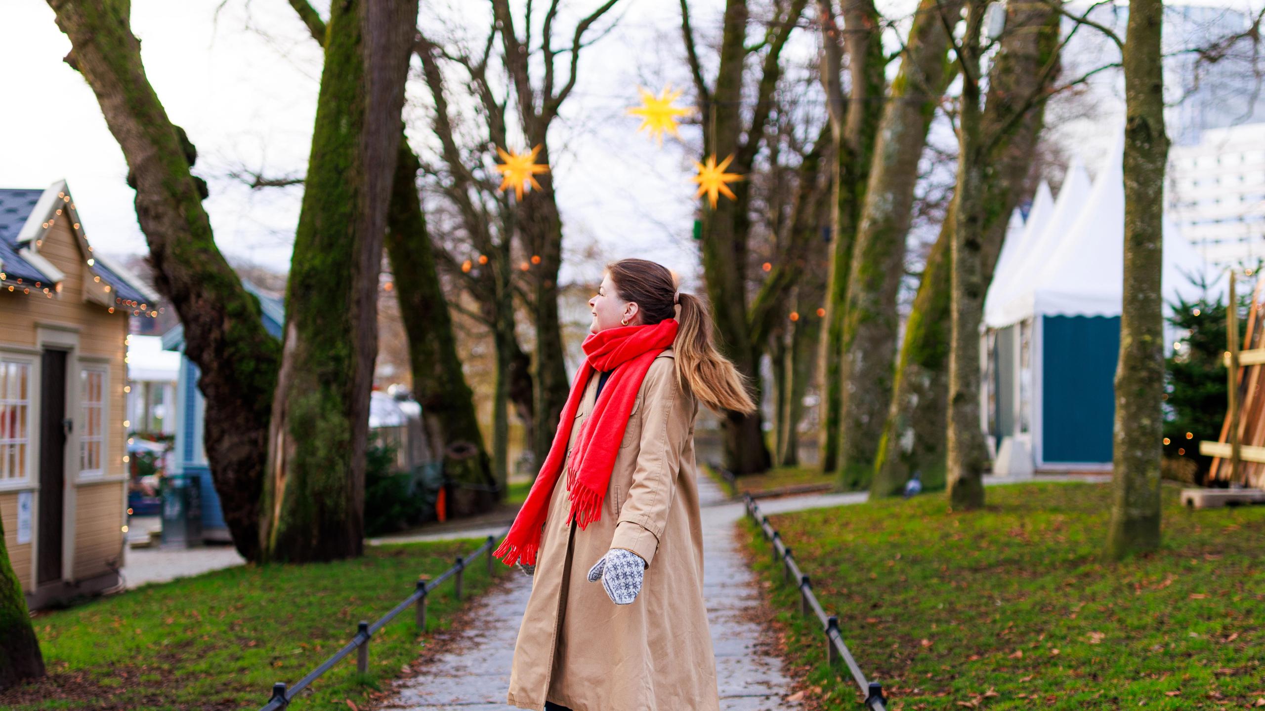 A woman strolling along a path in Stavanger, surrounded by trees decorated with yellow star-shaped lights, adding a festive, Christmas ambiance.