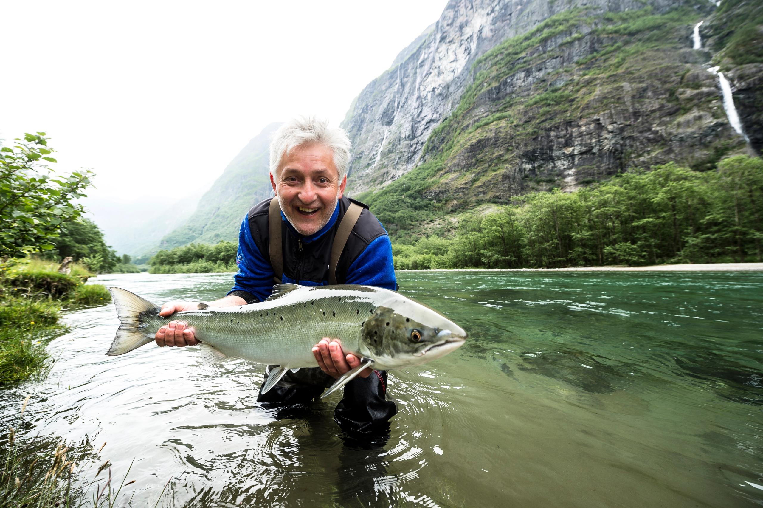 En sportsfisker står i Nærøydalselva på Vestlandet og holder opp en stor laks