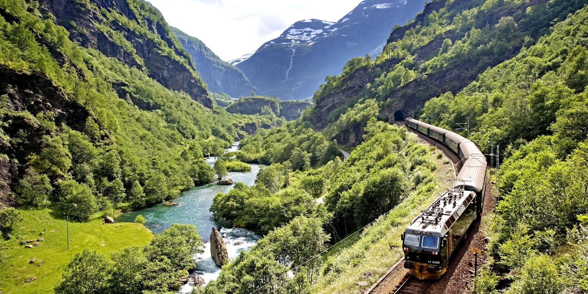 Un tren cruza un verde valle en Flåm en un día soleado.