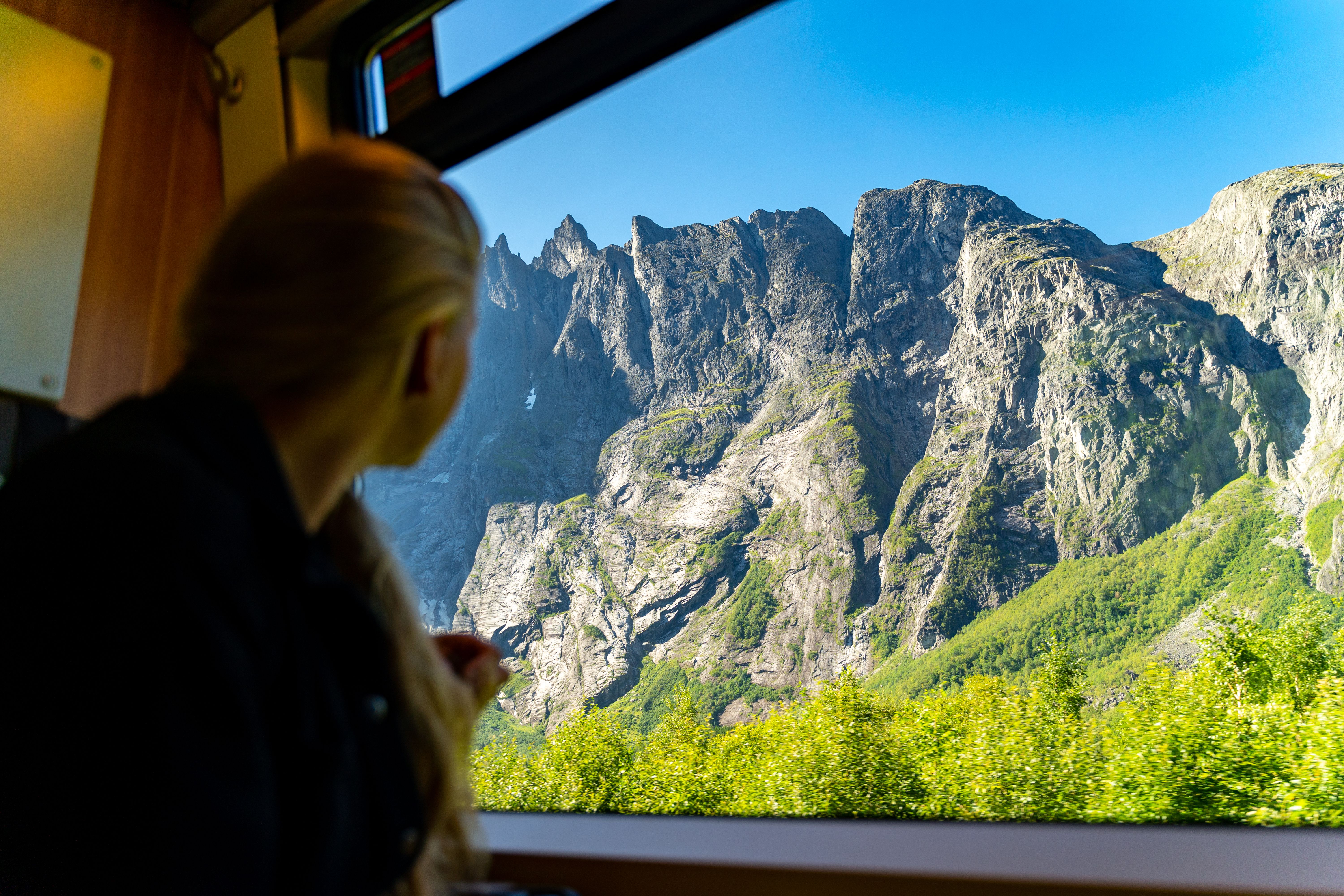 A woman looking through a train window at a towering mountain wall.