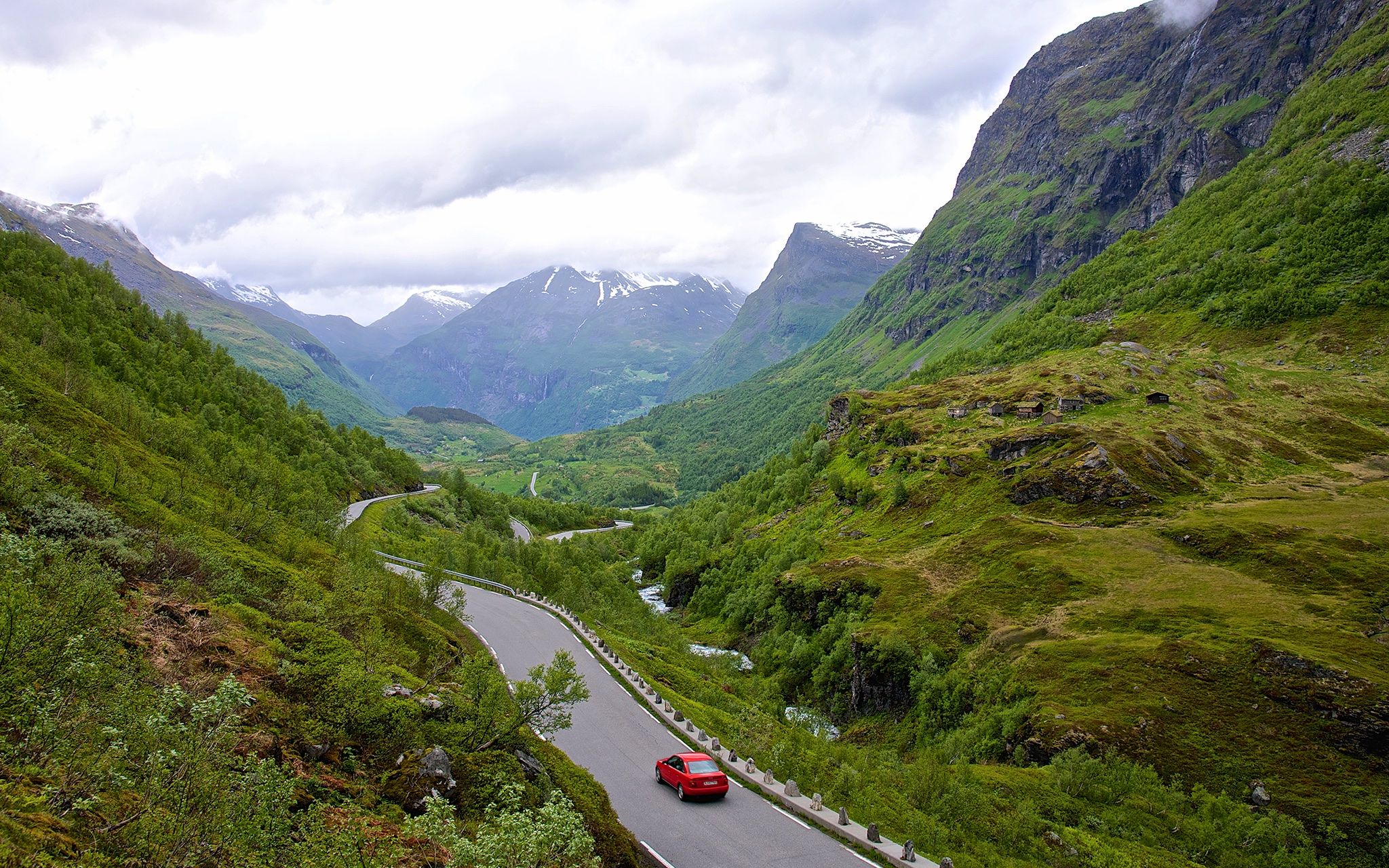 A red car driving on a small road in Geiranger, Norway