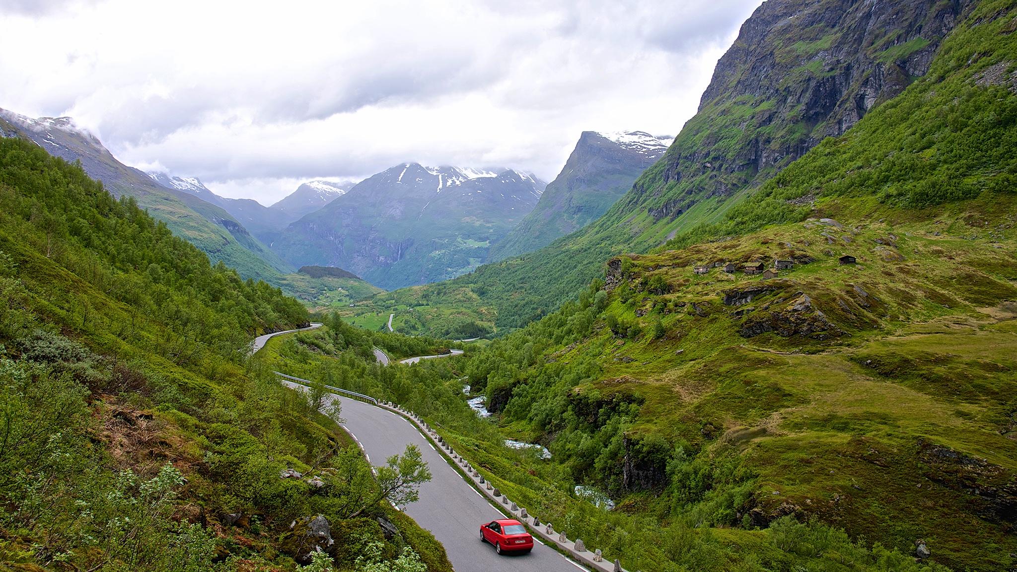 A red car driving on a small road in Geiranger, Norway