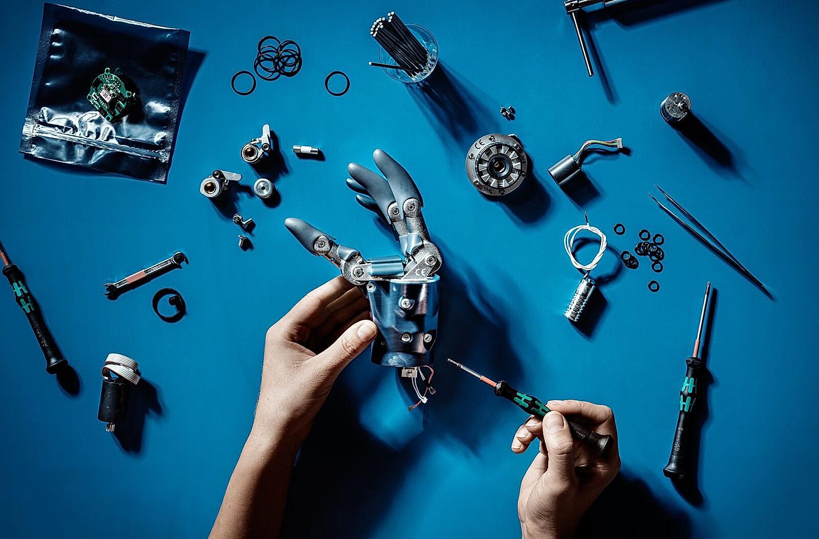 Two hands are working with tools to fix a robot arm
