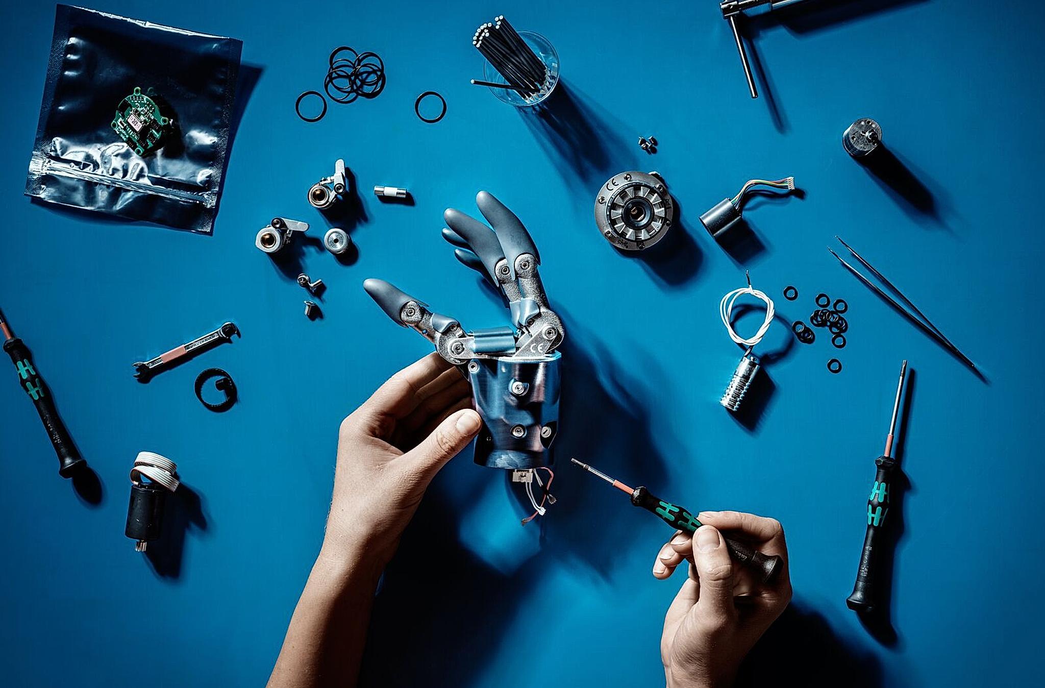 Two hands are working with tools to fix a robot arm