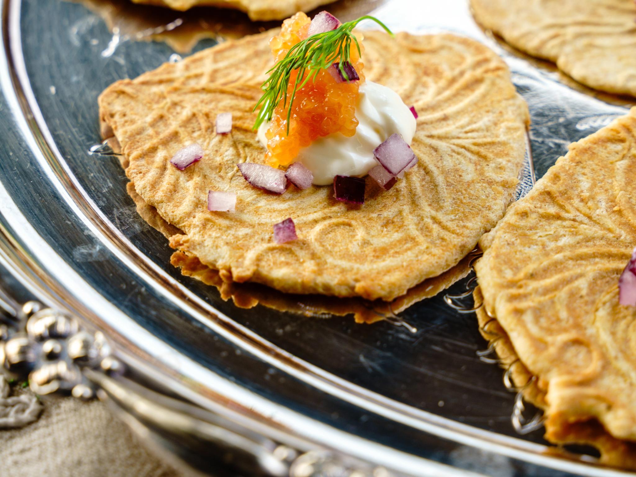 Krumkaker on a silver plate with salmon roe and sour cream.