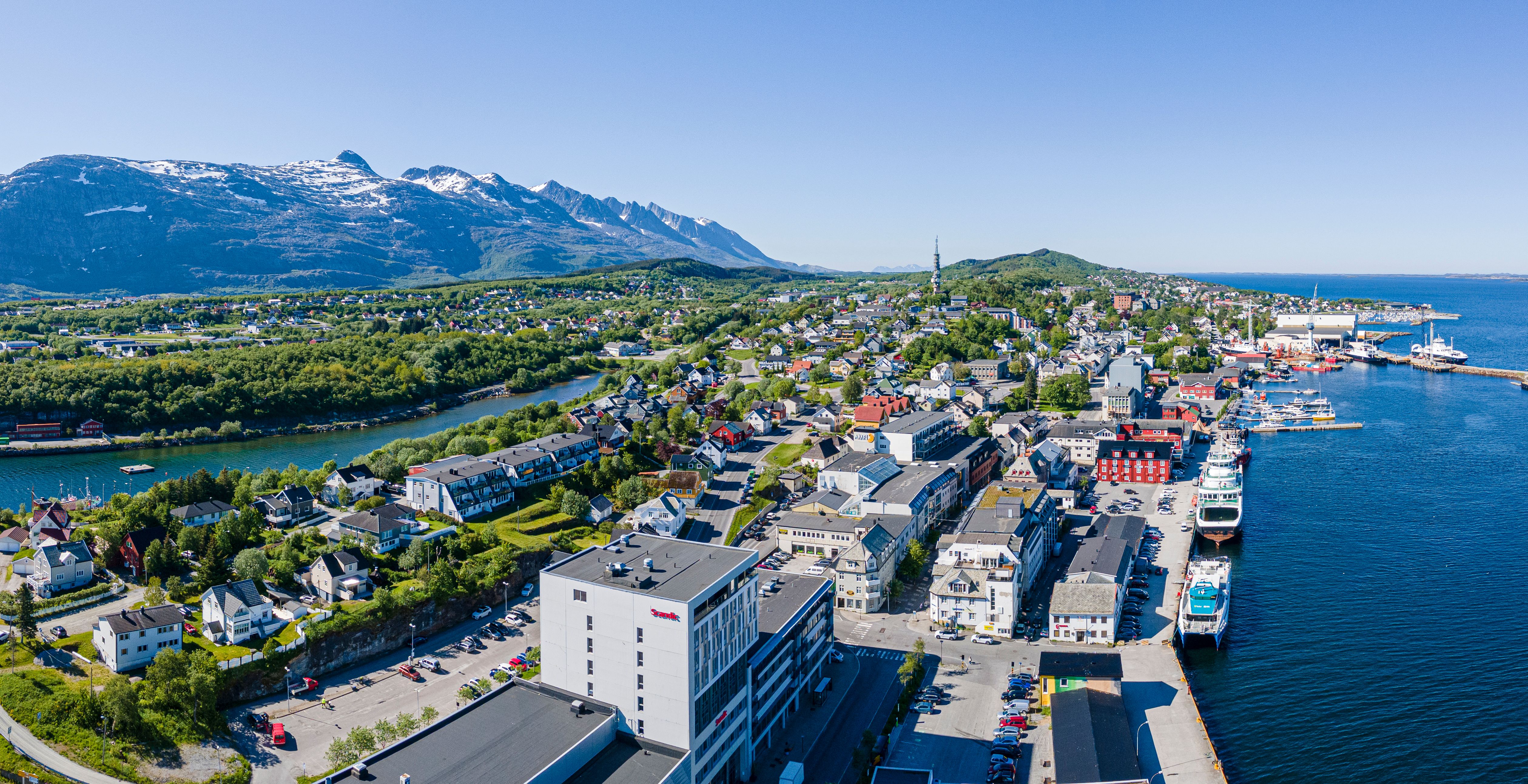 A panoramic view of a coastal city including mountains and the harbour.