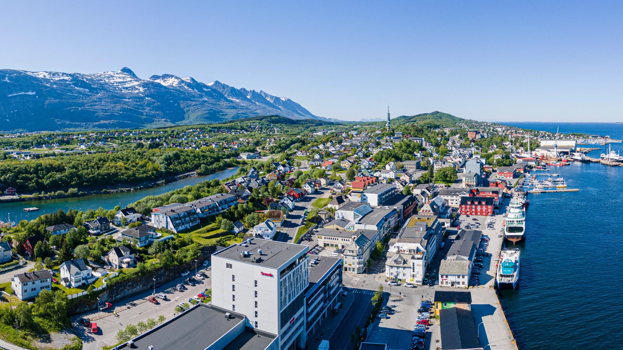 A panoramic view of a coastal city including mountains and the harbour.