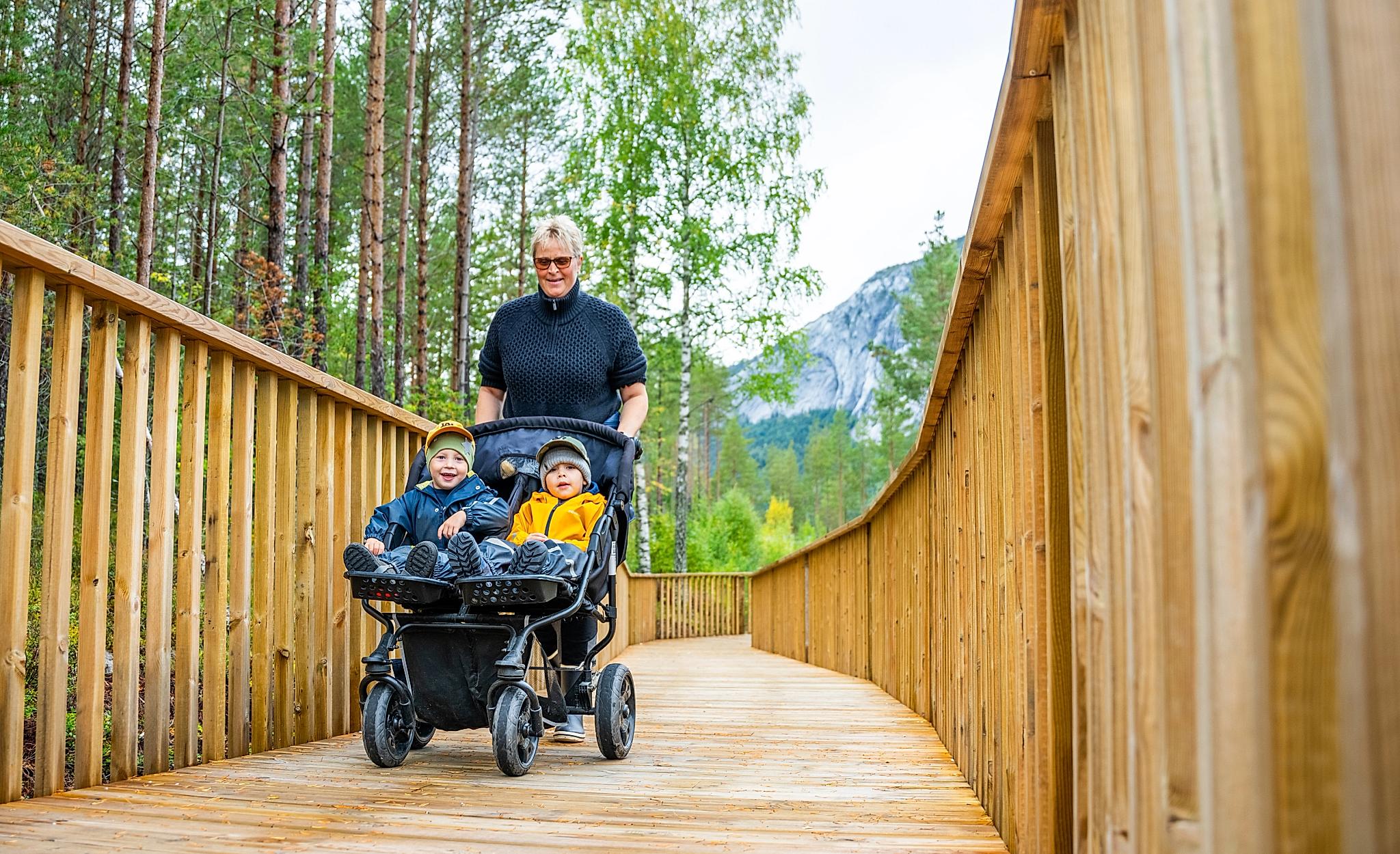 Person with two kids in a pram walking the treetop road in Fyresdal