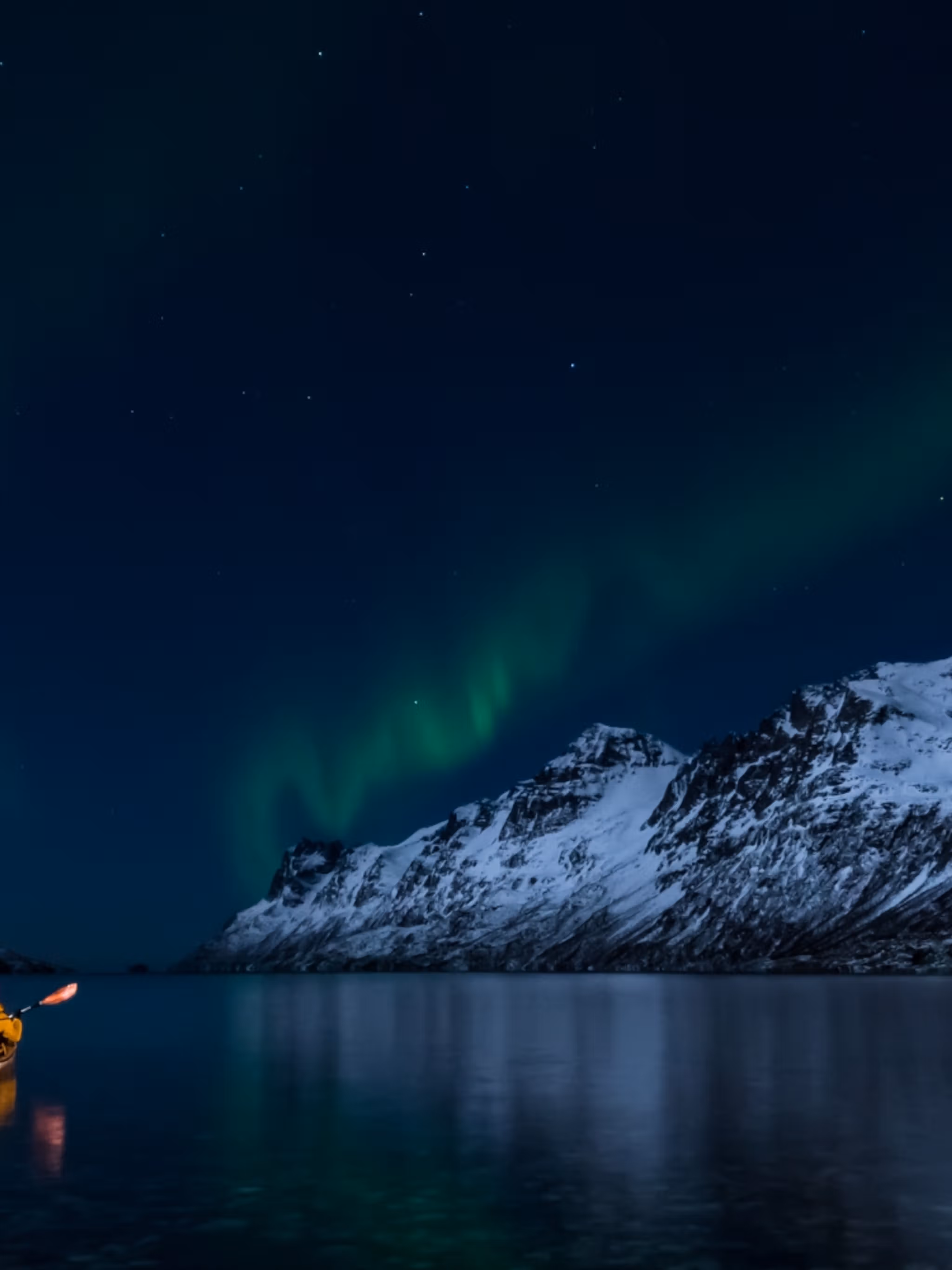 A woman paddling under the northern lights in Lofoten