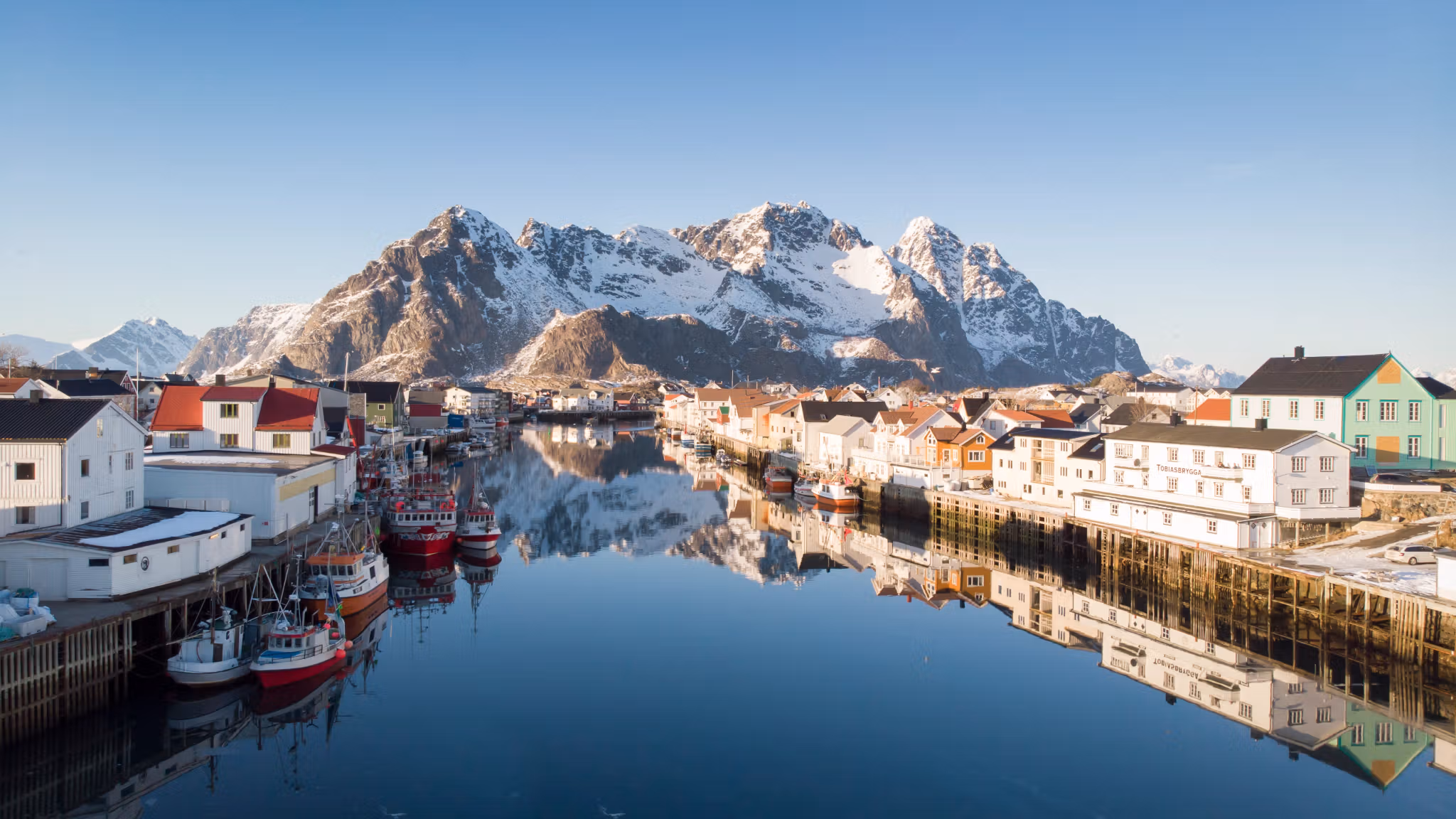 Houten huizen, vissersboten en besneeuwde bergen in Henningsvær op de Lofoten in Noord-Noorwegen op een zonnige winterdag