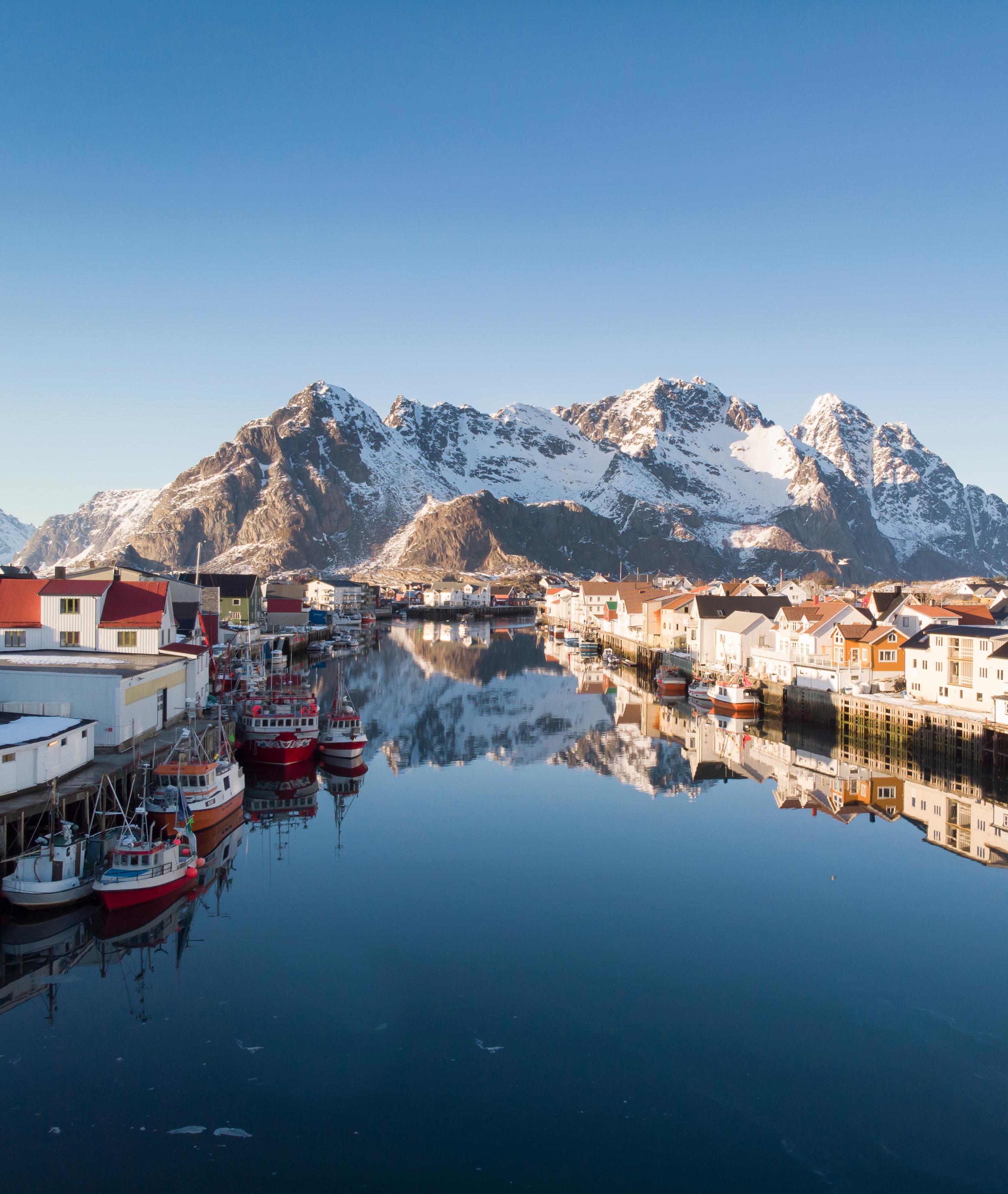 Wooden houses, fishing boats and snowcapped mountains, Henningsvær in certified Sustainable Destination Lofoten, Northern Norway