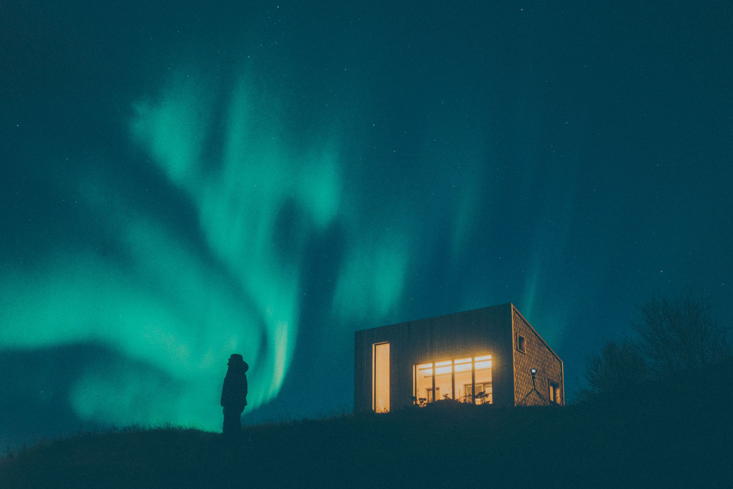 A person watching the green northern lights next to a building in Bodø, Northern Norway