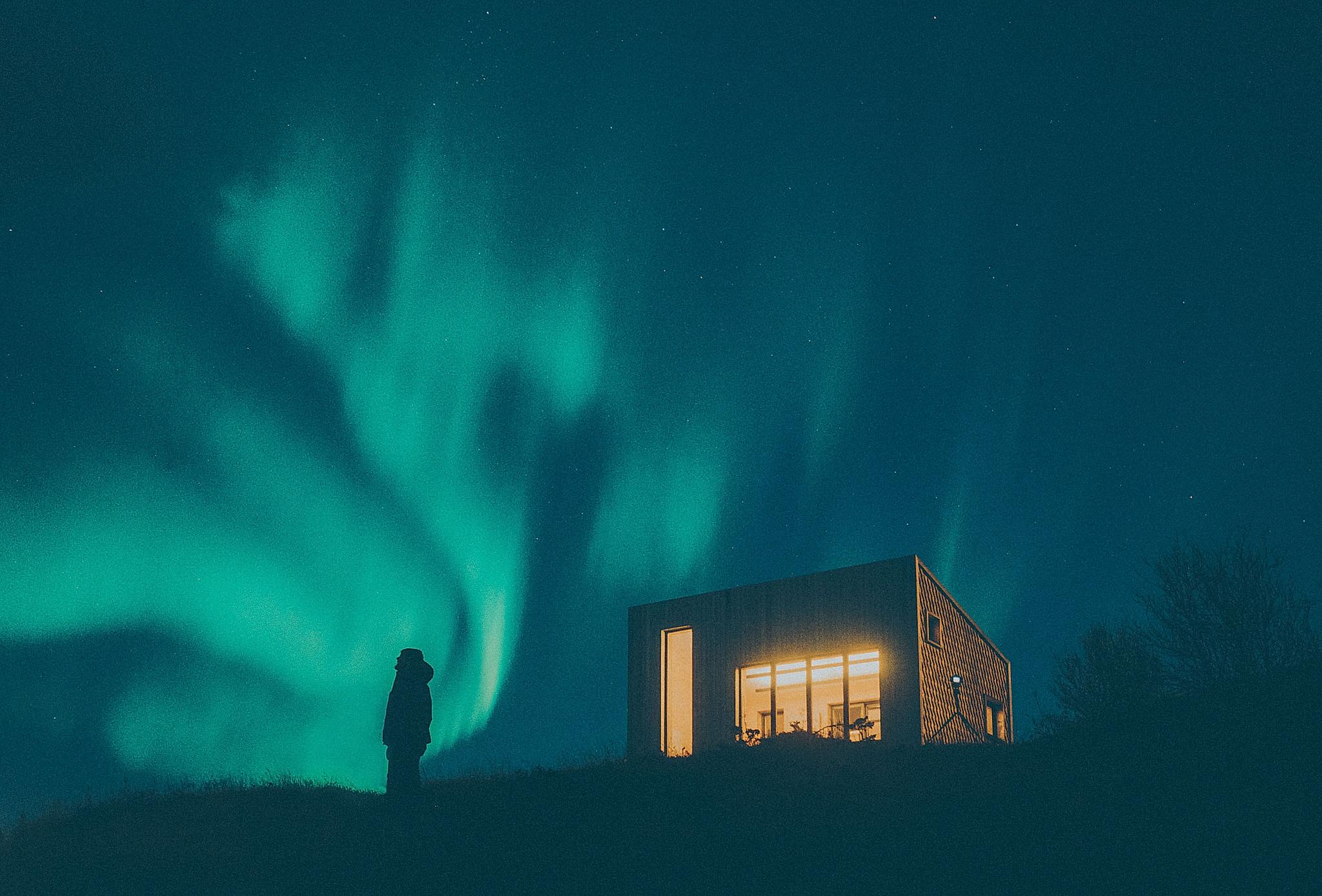 A person watching the green northern lights next to a building in Bodø, Northern Norway