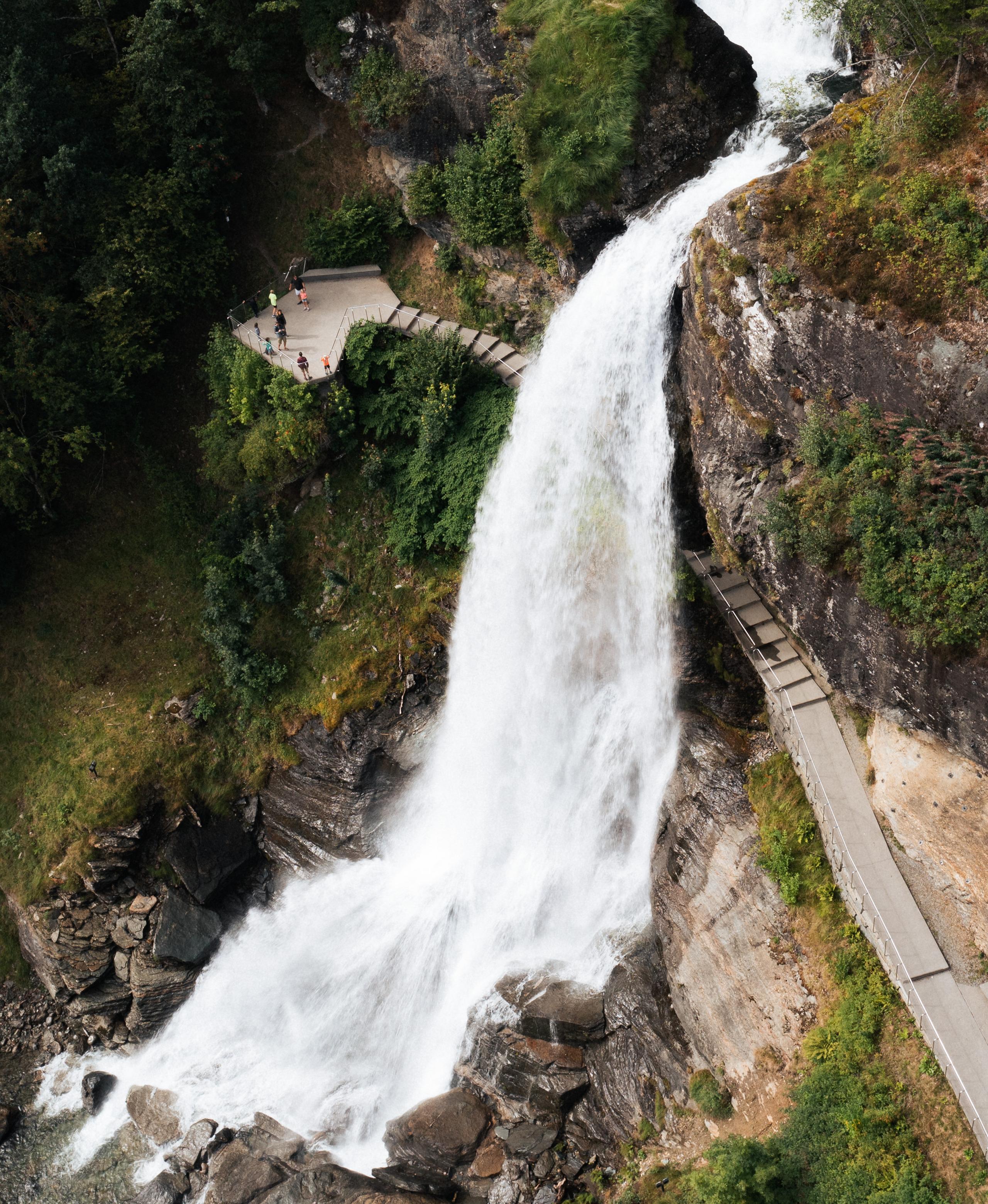 A water fall rushing down a mountain with people walking behind it.