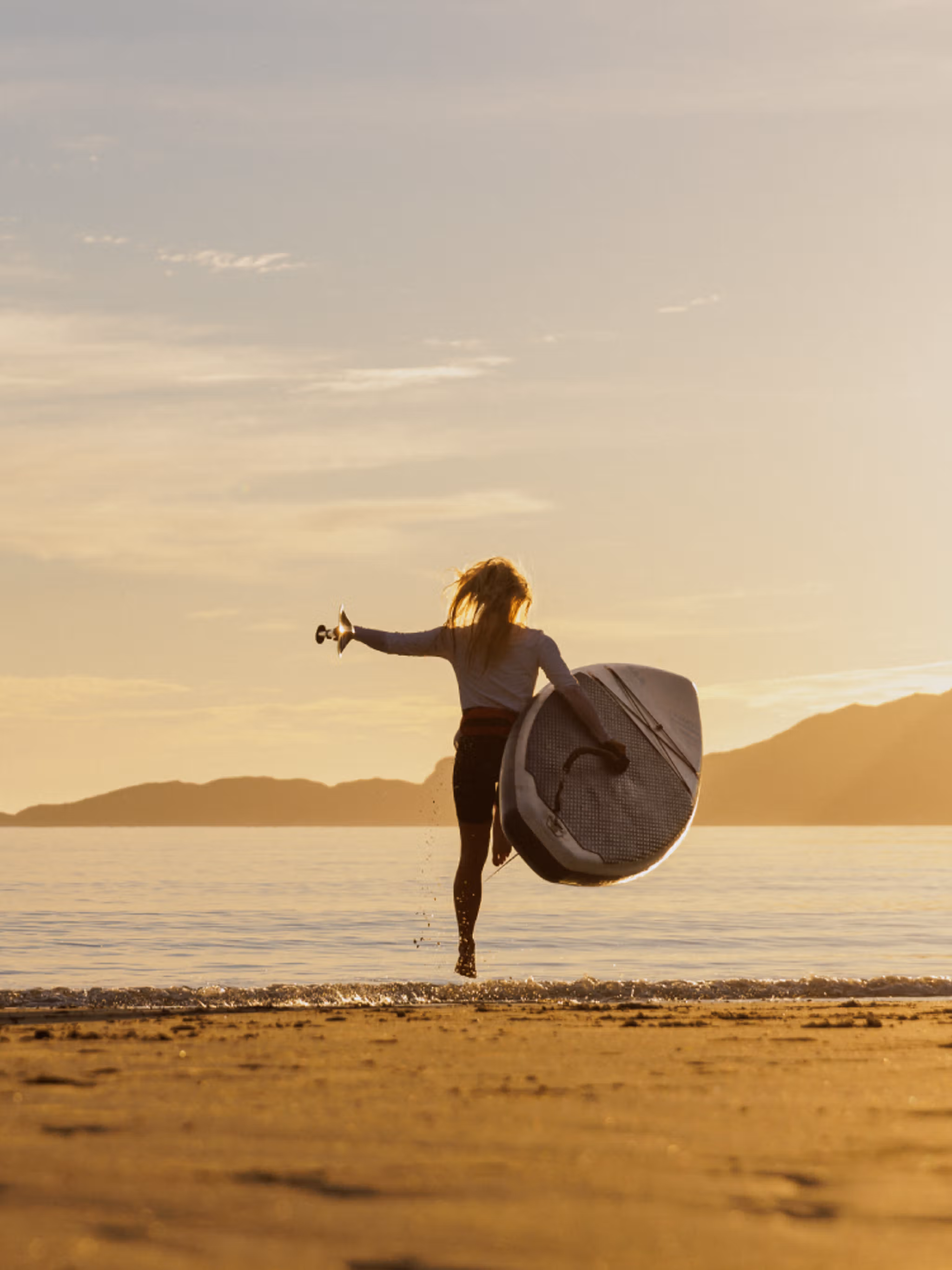 A woman going out in the water with a paddle board in the midnight sun, Northern Norway.