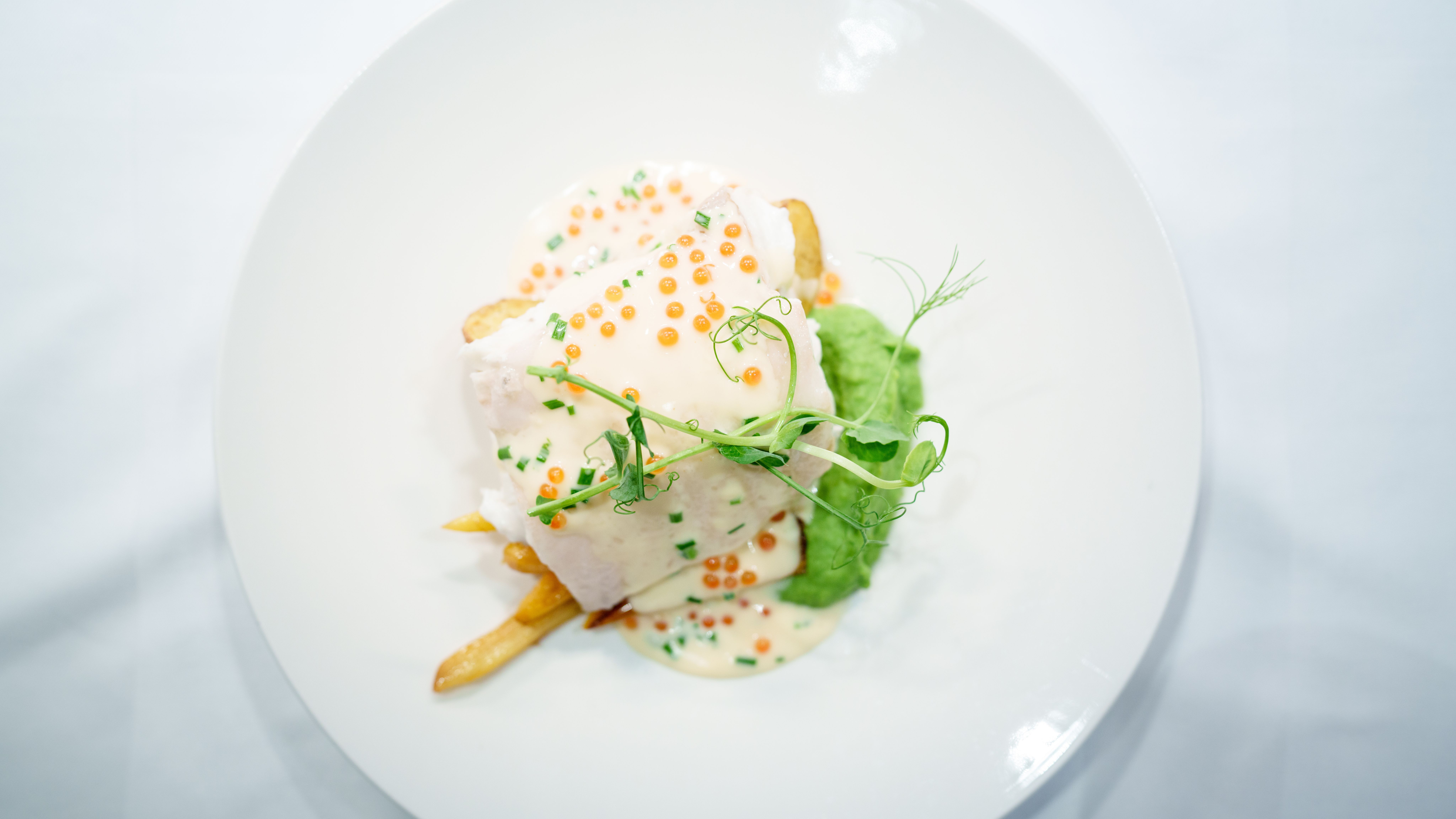 A plated dish of halibut, potatoes, pea puree and a white sauce.