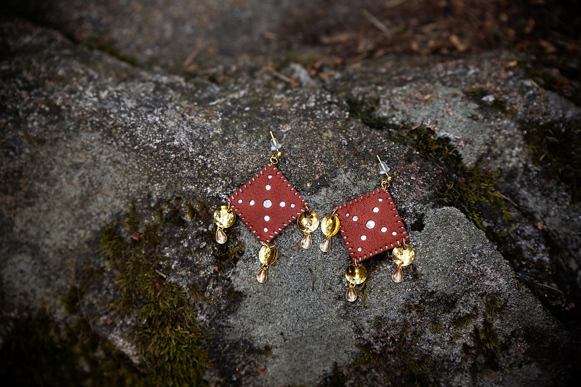Leather and gold Sami inspired earrings resting on a rock