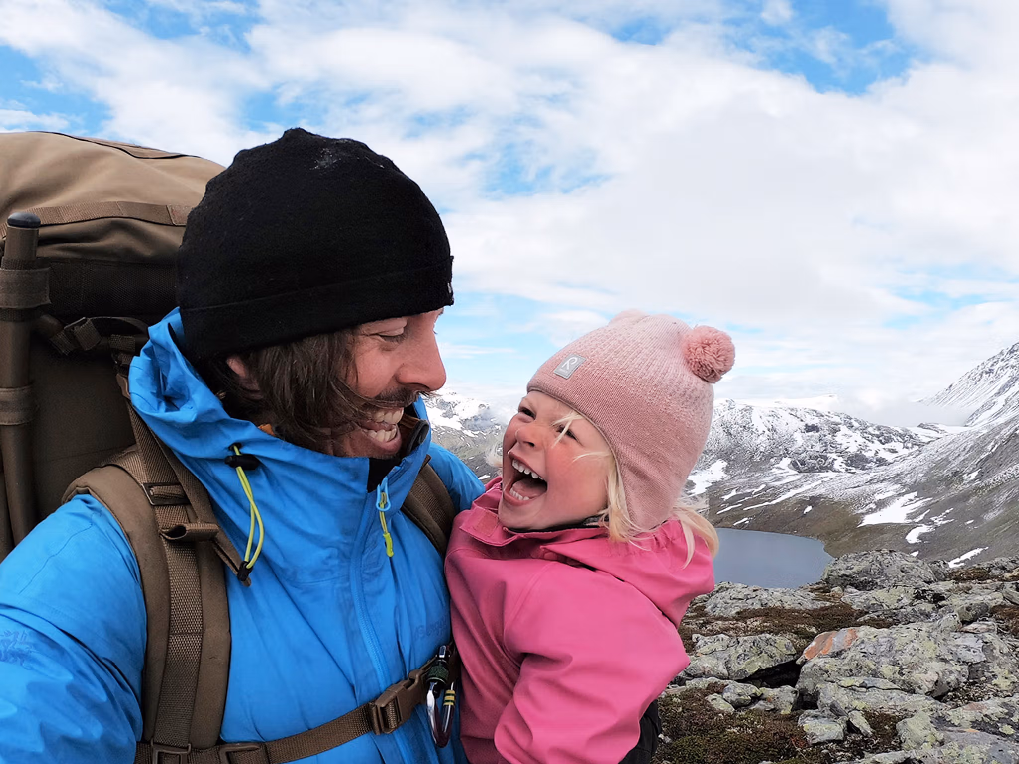 Nærbilde av en ung jente og pappaen hennes som smiler til hverandre på vandretur i Hjørundfjorden på Vestlandet