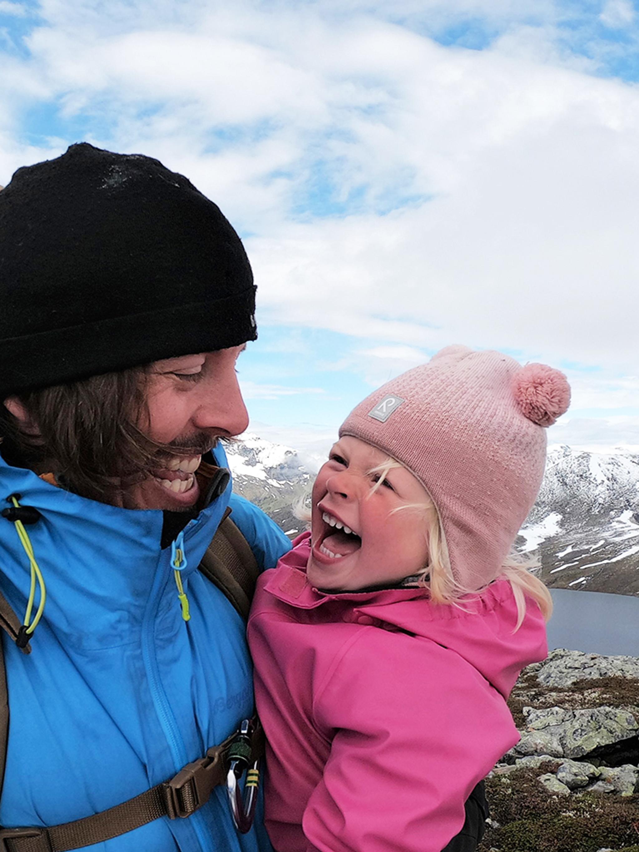 Close-up van een jong meisje en haar vader die naar elkaar lachen tijdens een wandeltocht in Hjørundfjorden, Fjord-Noorwegen.