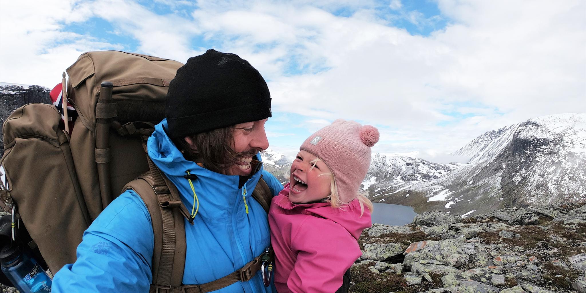 Nærbilde av en ung jente og pappaen hennes som smiler til hverandre på vandretur i Hjørundfjorden på Vestlandet