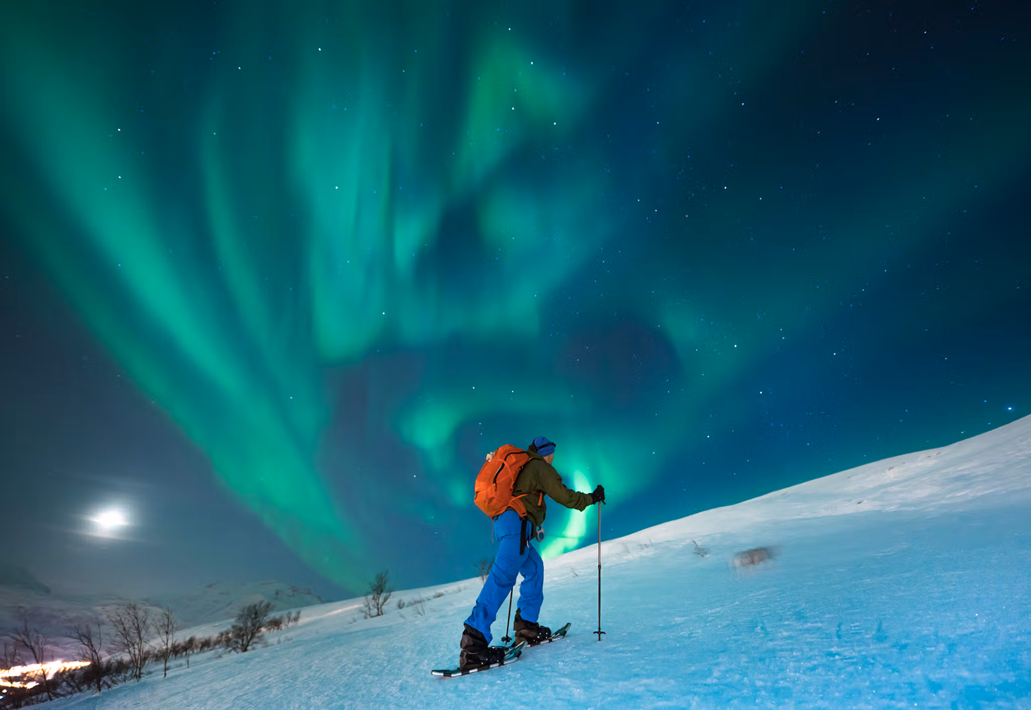 A person snowshoeing under the northern lights in Tromsø, Northern Norway
