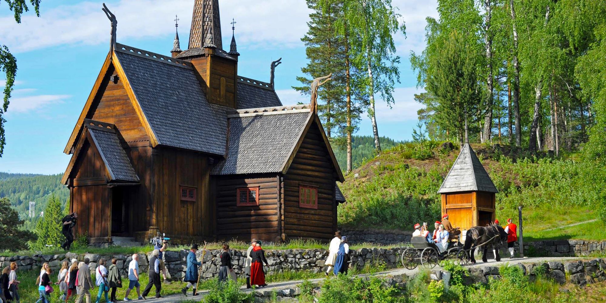 Un grupo de personas vestidas con trajes típicos, delante de la iglesia medieval de Maihaugen, en Lillehammer, Este de Noruega.