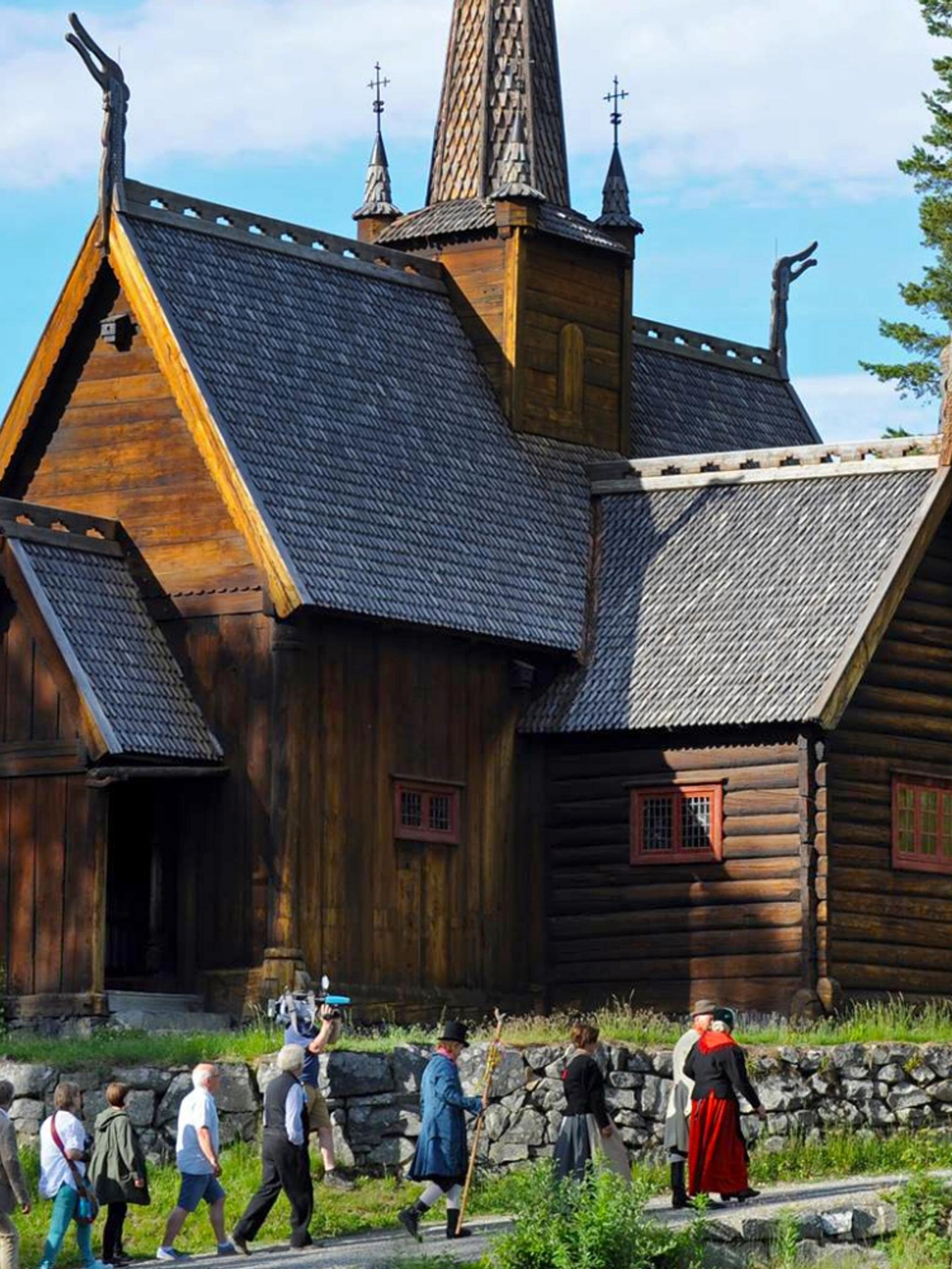 Un grupo de personas vestidas con trajes típicos, delante de la iglesia medieval de Maihaugen, en Lillehammer, Este de Noruega.