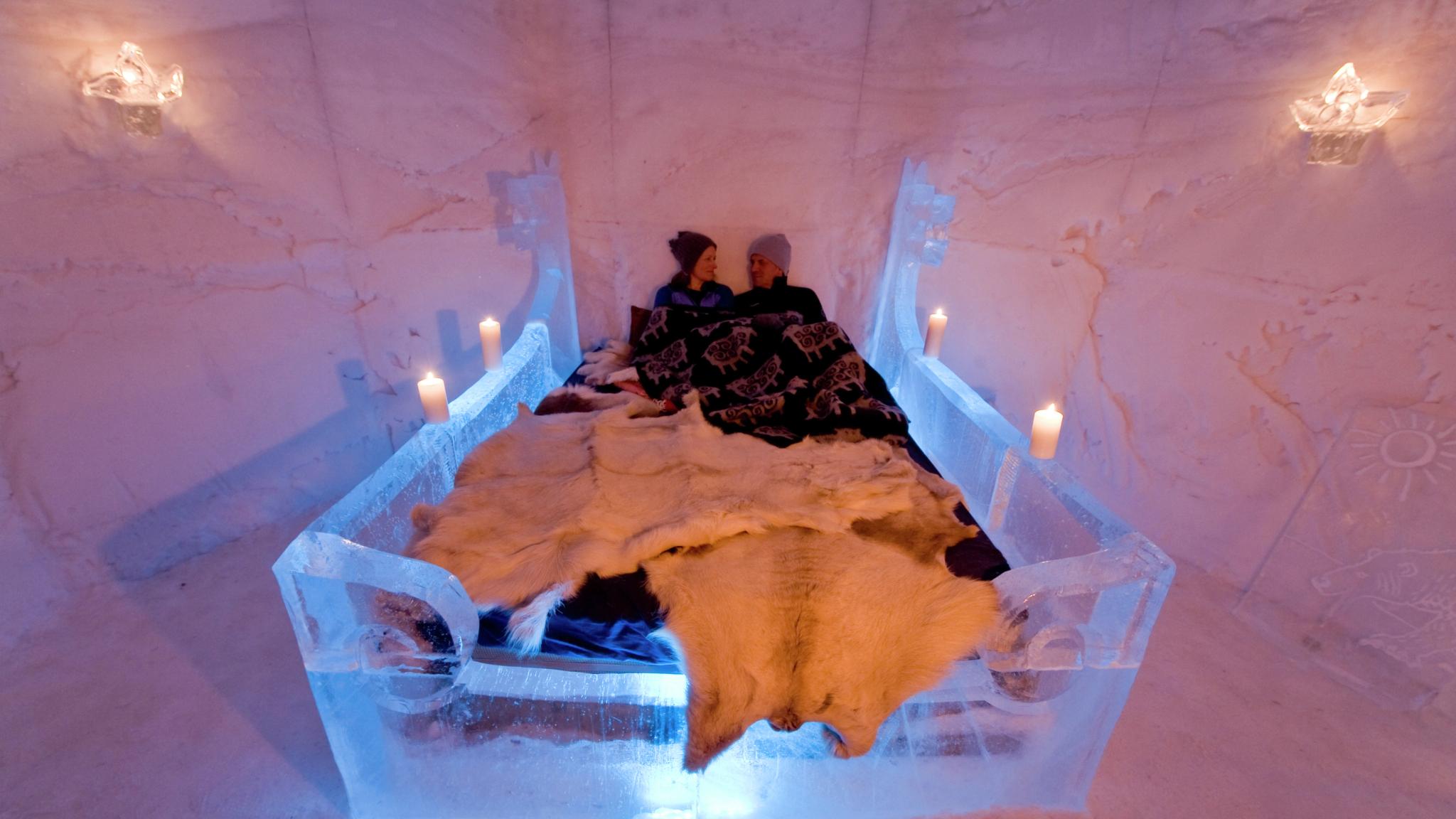 Two people in a bed with reindeer blankets in Sorrisniva Igloo Hotel, Northern Norway