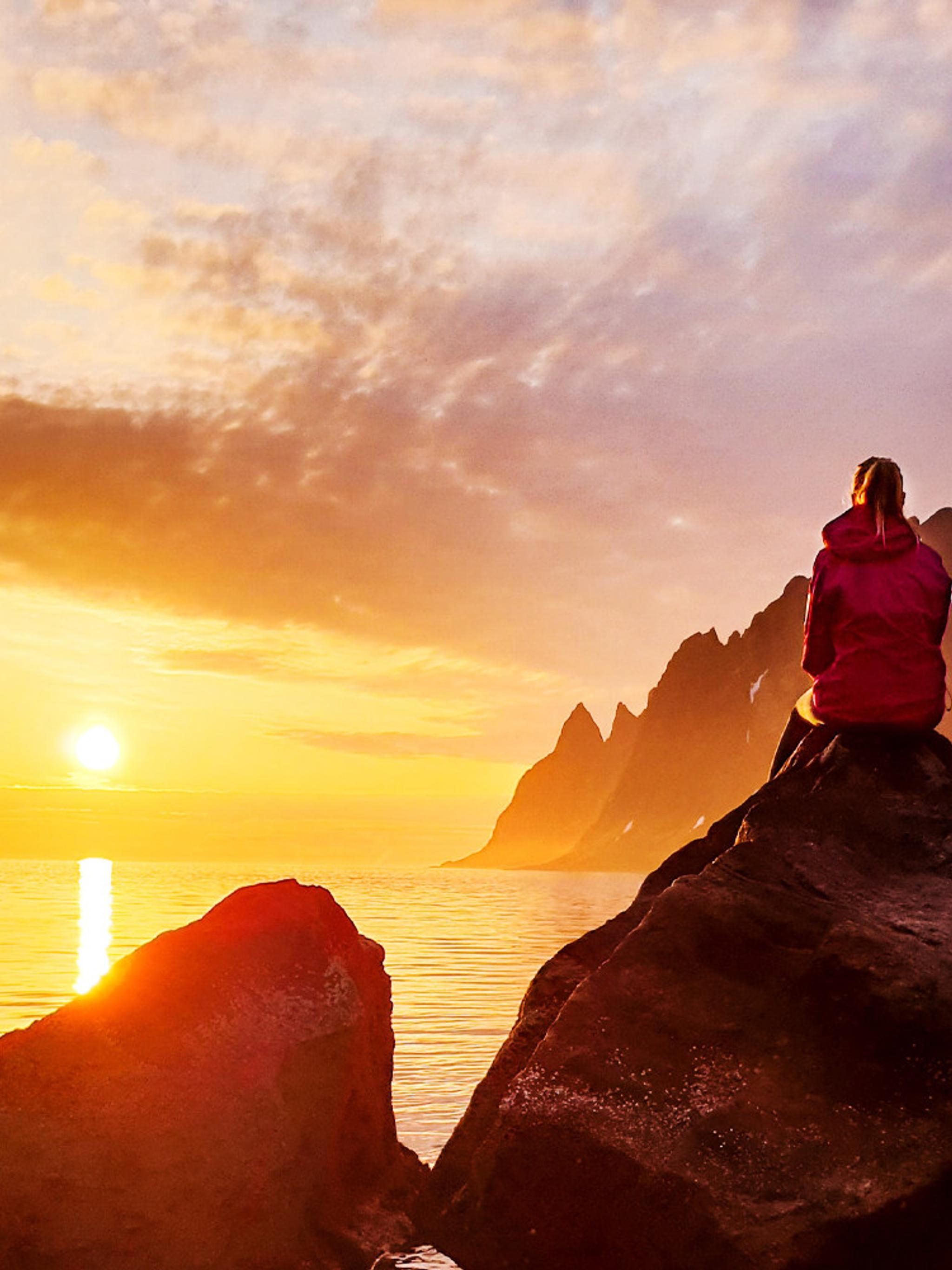 En person ser på midnattssola på Senja i Nord-Norge