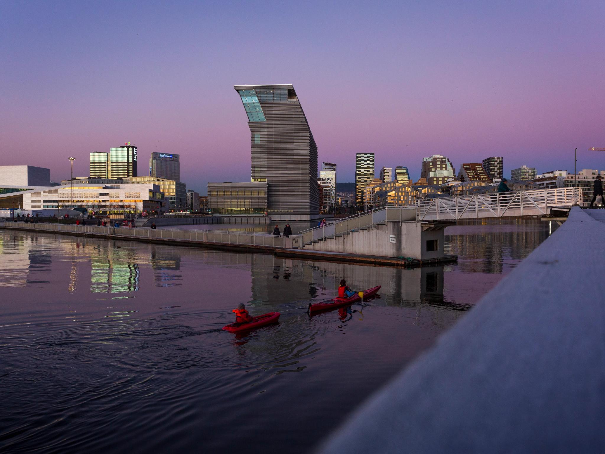 Two people in kayaks in front of the new Deichman main library in Oslo in a purple sunset