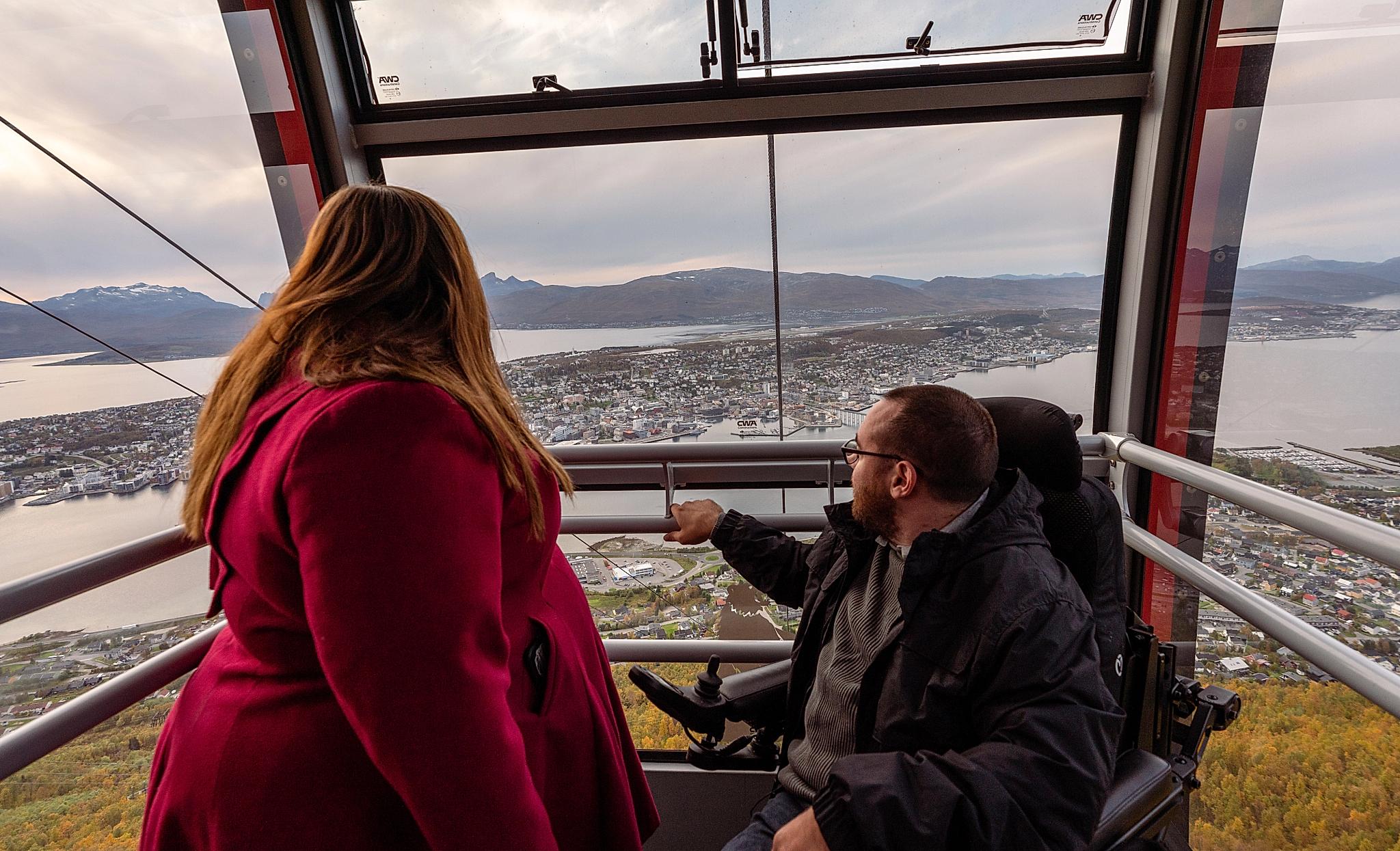 En kvinne og en handikappet mann tar Fjellheisen opp Storsteinen i Tromsø