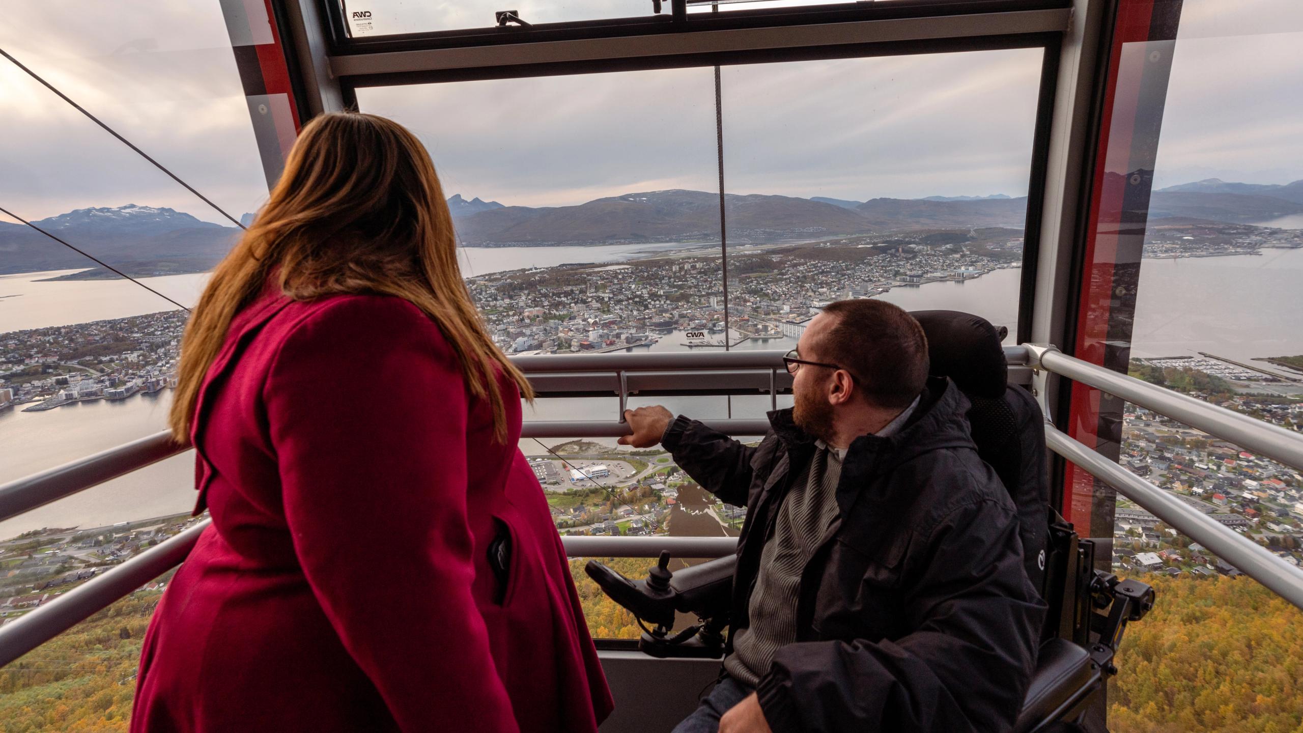 En kvinne og en handikappet mann tar Fjellheisen opp Storsteinen i Tromsø