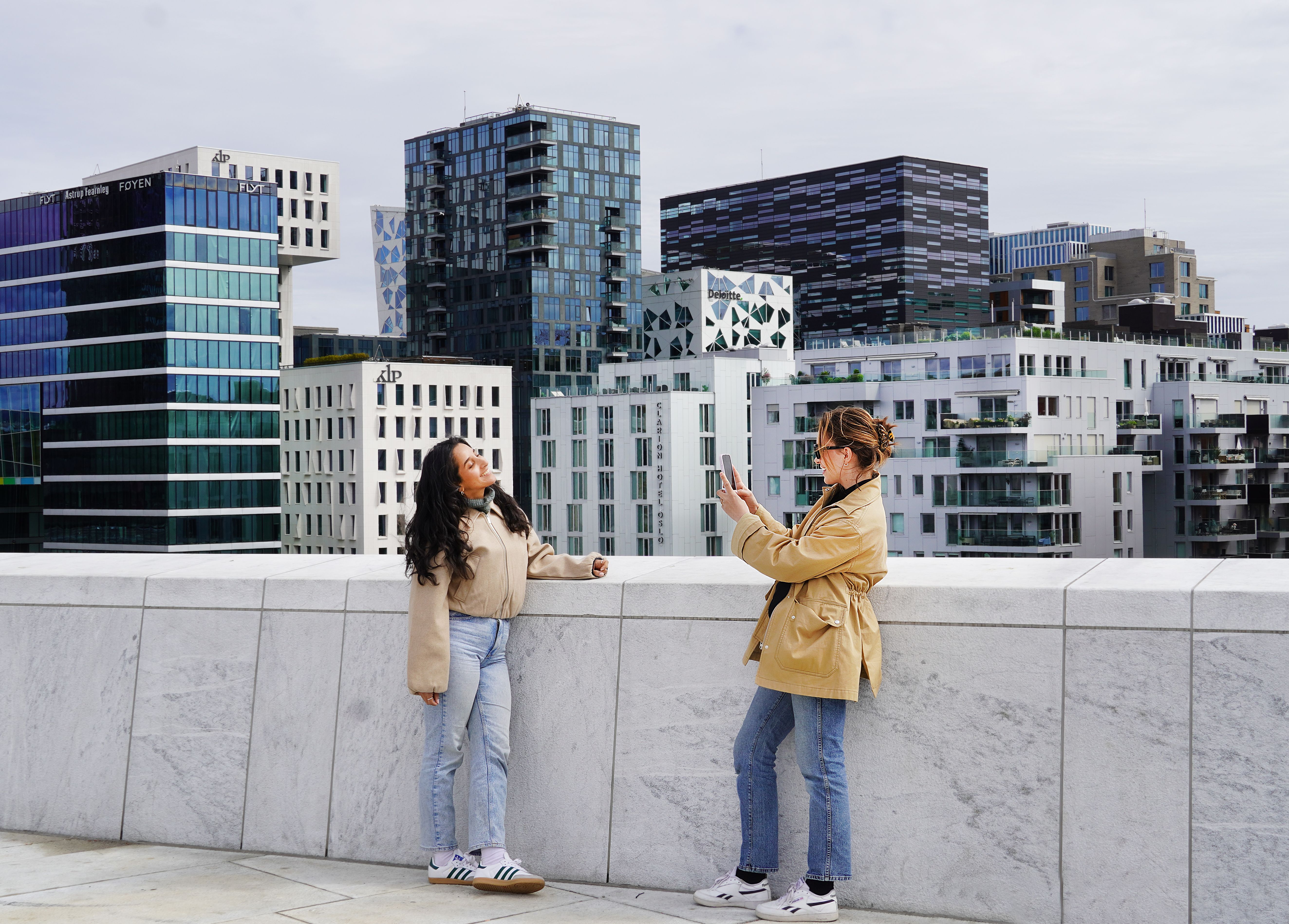 Two young women standing on the rooftop of the Oslo Opera House in Norway, capturing a photo with the city skyline in the background