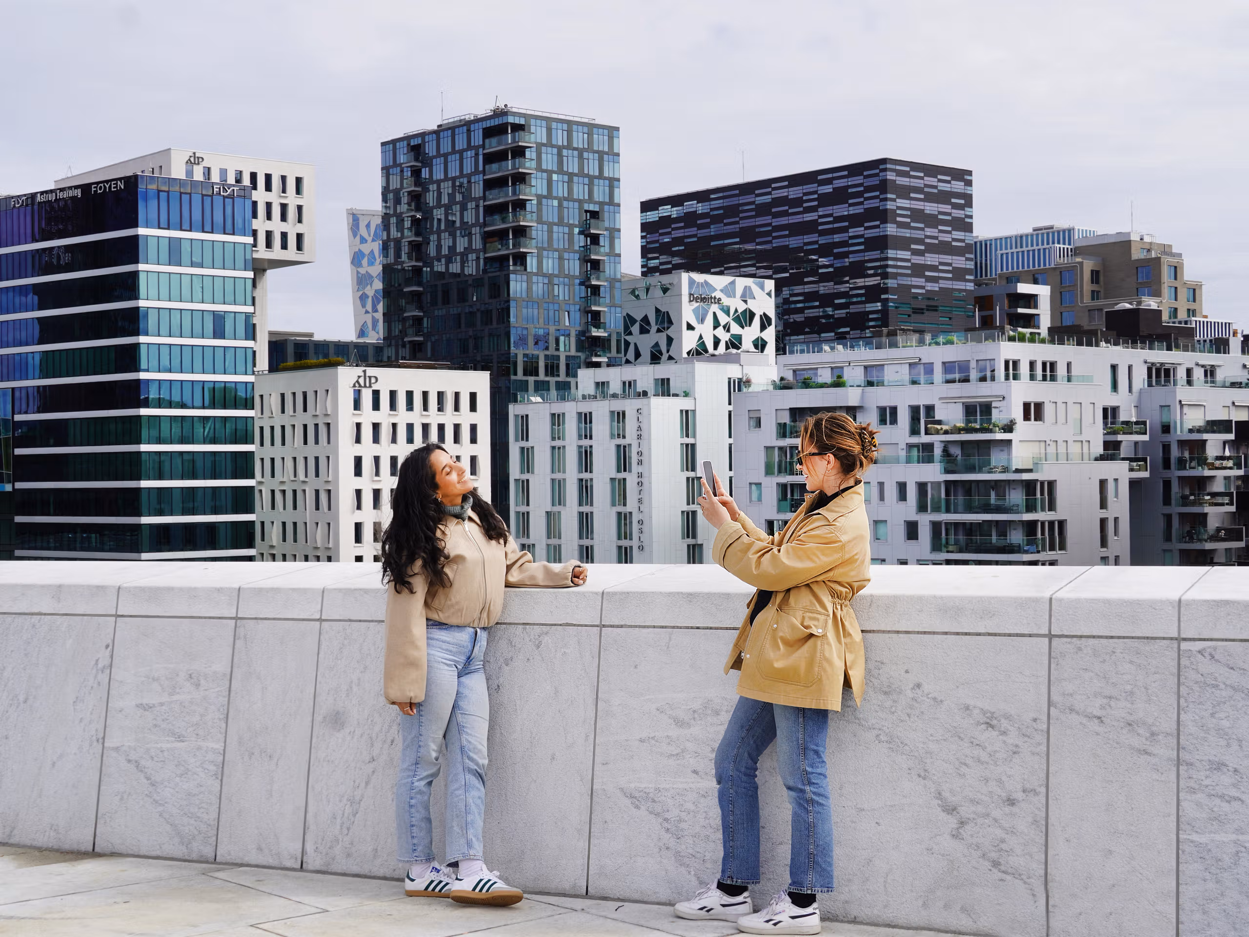 Two young women standing on the rooftop of the Oslo Opera House in Norway, capturing a photo with the city skyline in the background