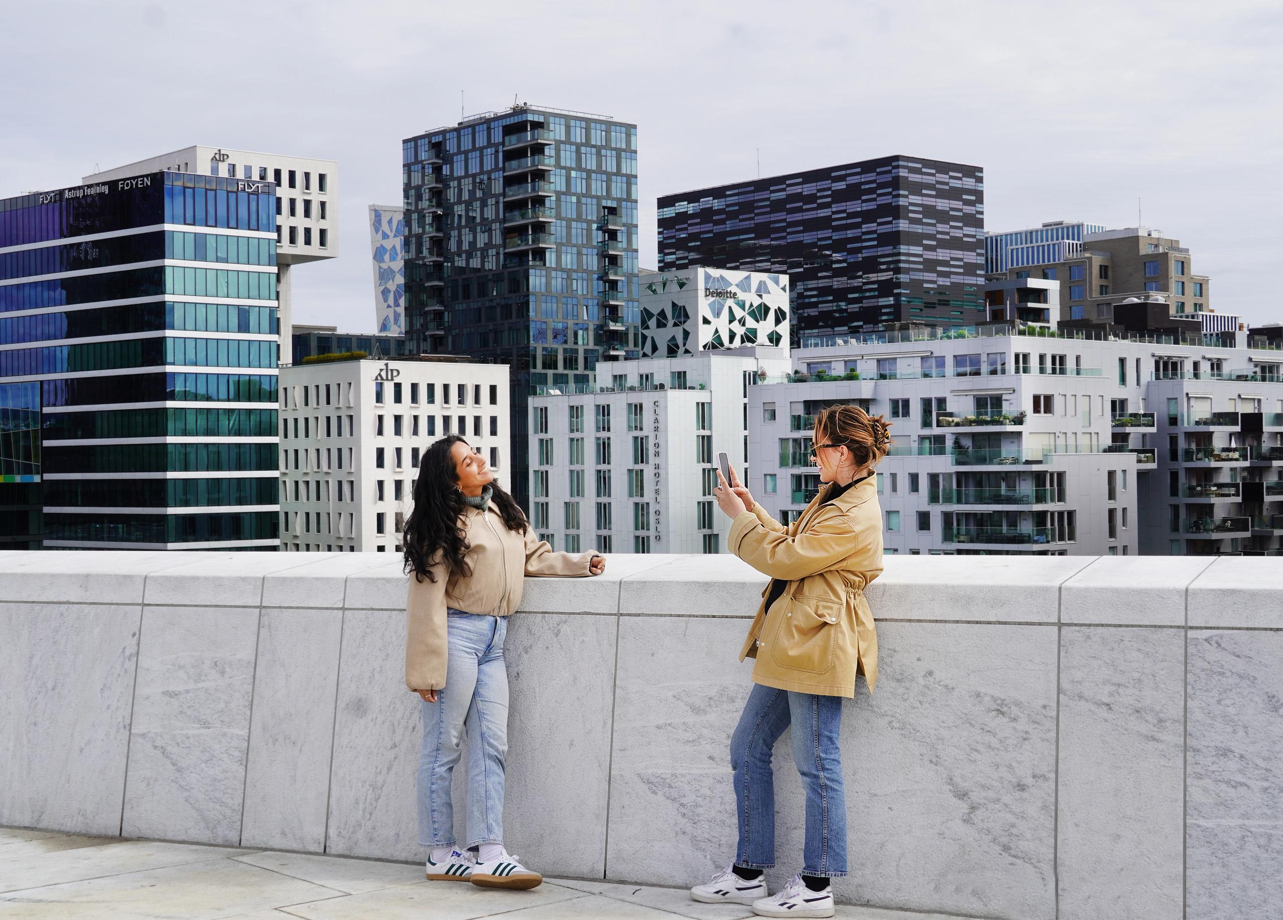 To unge kvinner står på taket av Operahuset i Oslo og tar et bilde, med Barcode i bakgrunnen