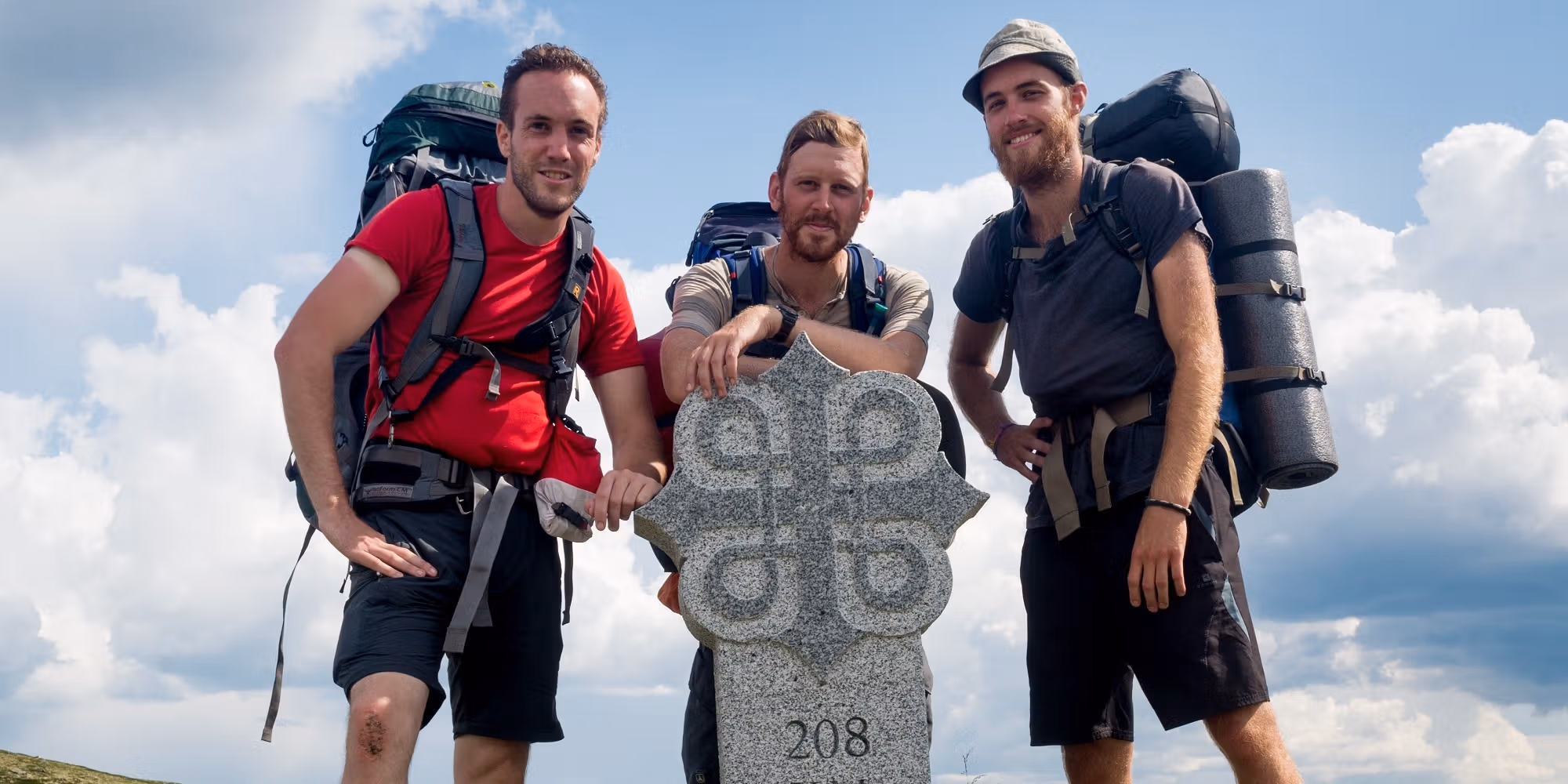 Three men standing around a milestone on the pilgrimage path to Trondheim, Norway