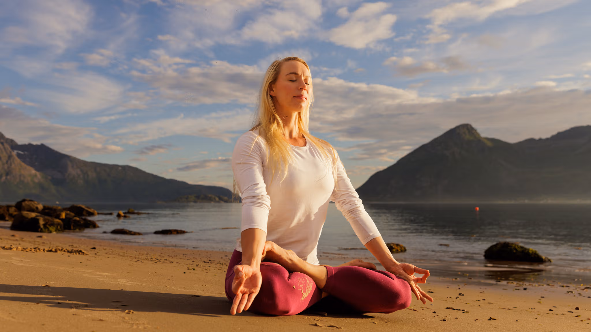 A woman sitting in lotus yoga position on the beach in the midnight sun, Northern Norway.